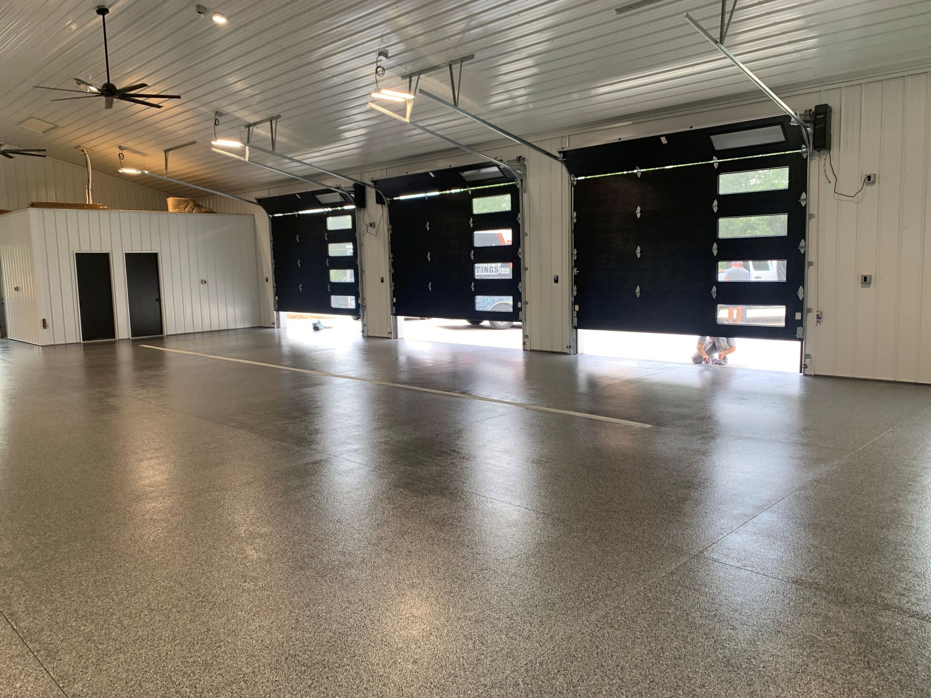 Empty industrial garage with polished concrete floor, white walls, and large black bay doors