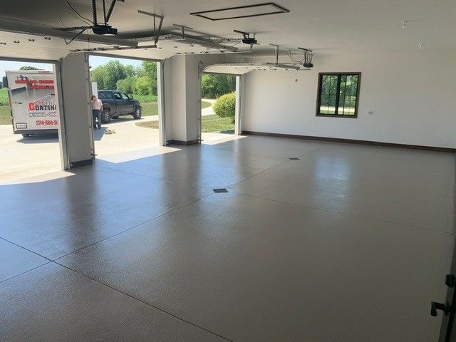 Empty garage interior with smooth gray floor, open doors, and daylight coming in