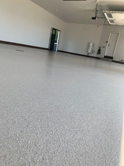 Empty room with speckled floor, white walls, and a door in the background.