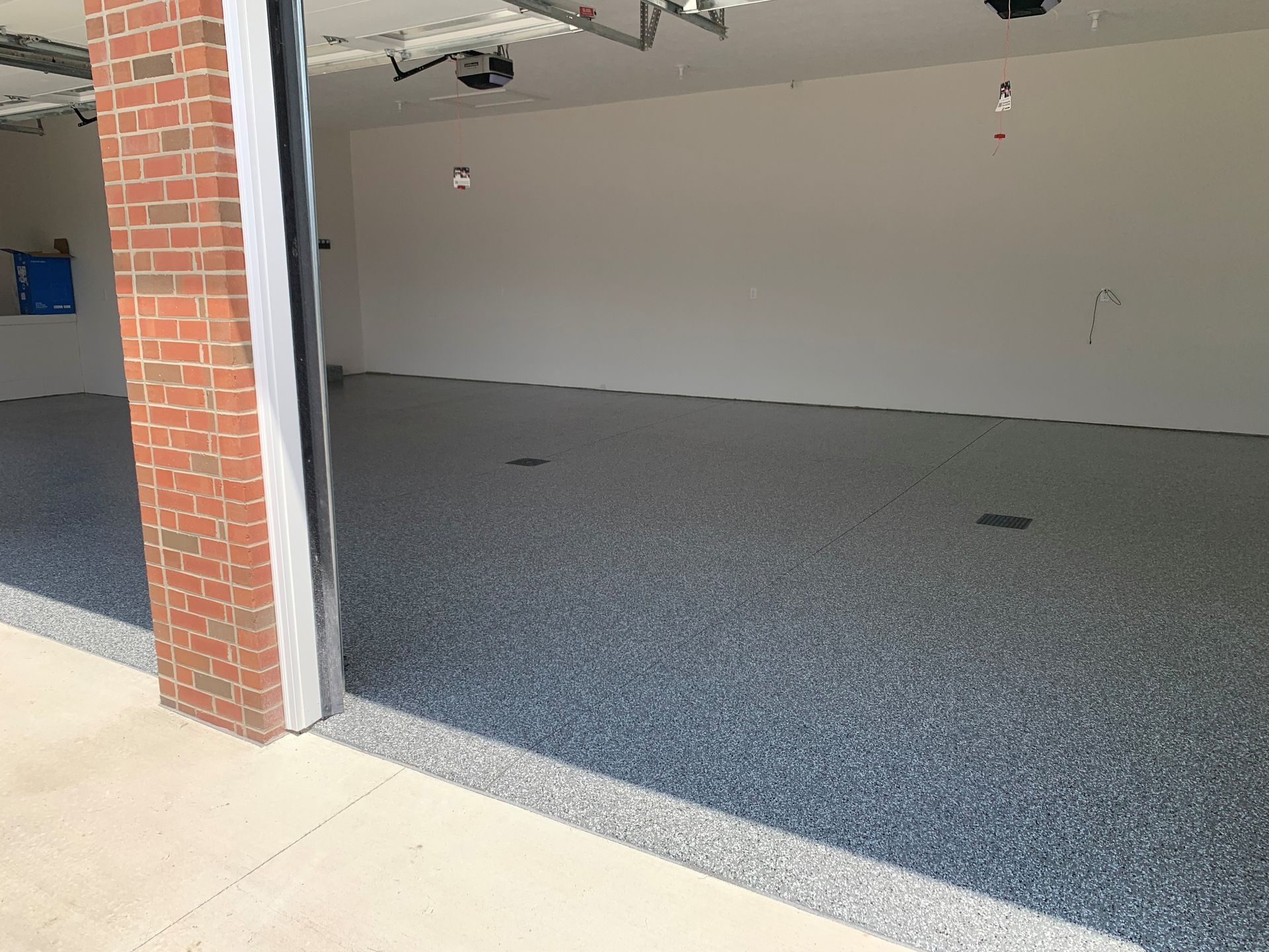Empty garage with gray speckled floor and open door, viewed from the driveway