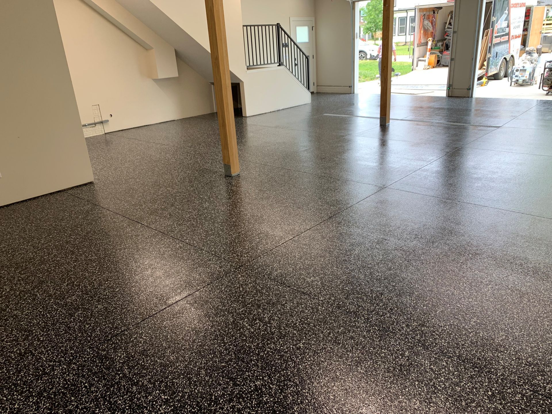 Empty indoor space with speckled epoxy floor, wooden support posts, and an open doorway to the outside