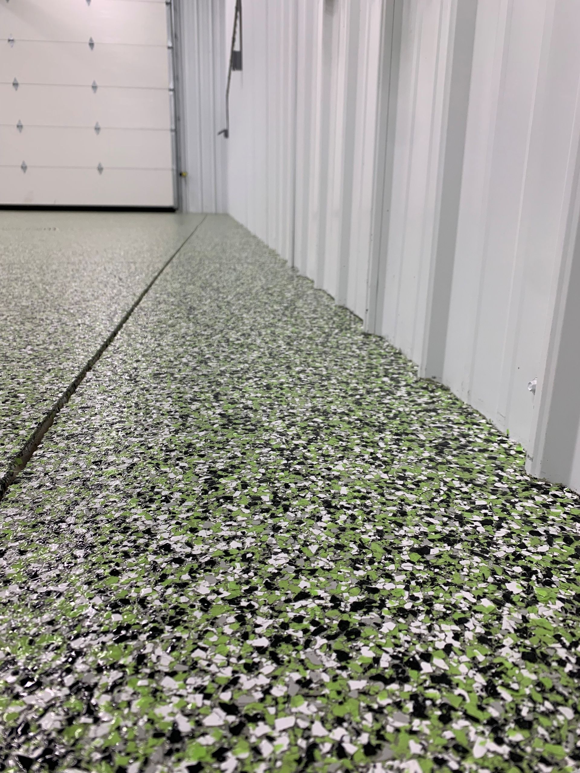 White metal wall beside a speckled green, white, and black textured floor in an industrial interior