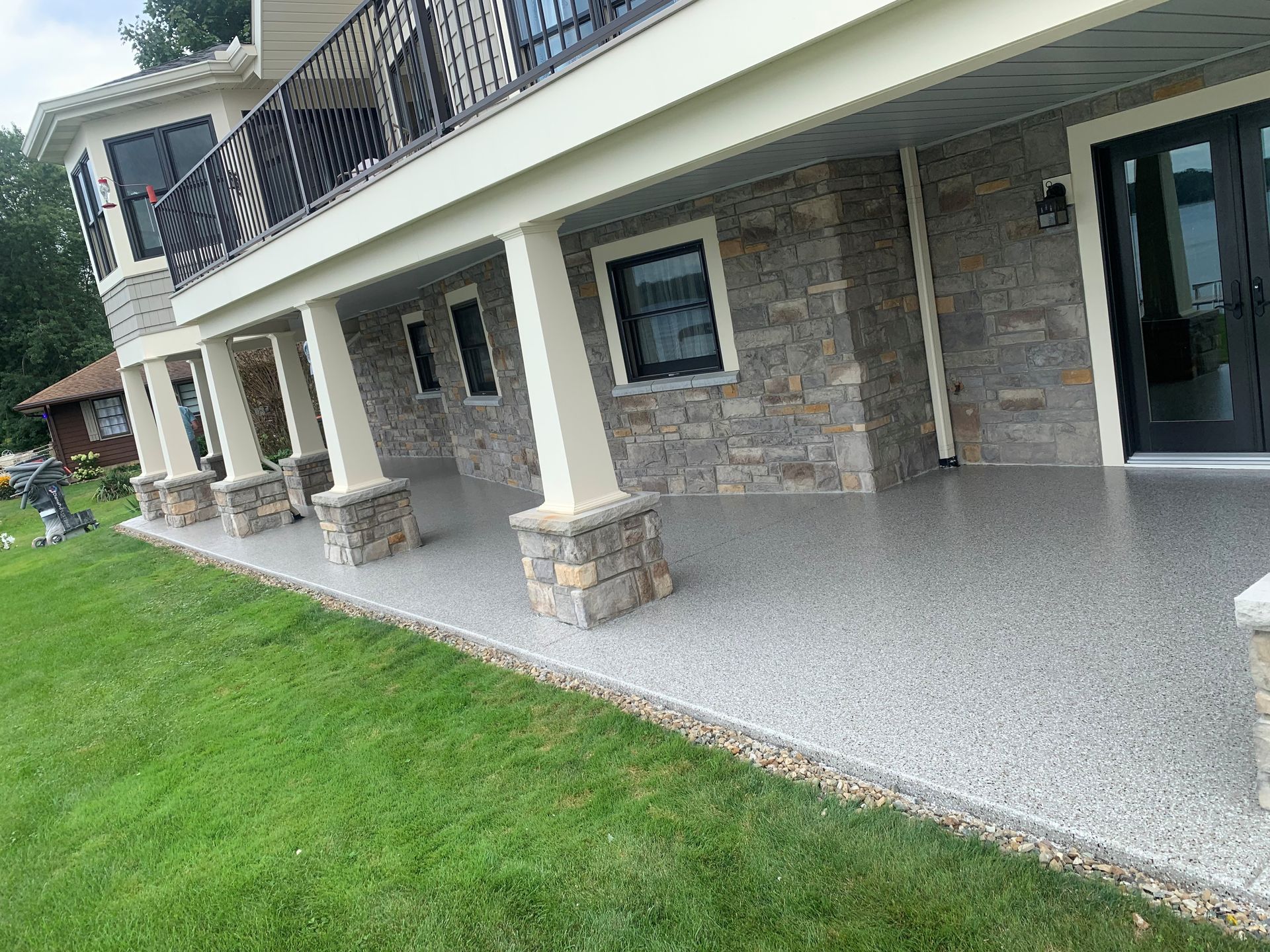 Stone-sided house with covered patio, balcony, and green lawn.