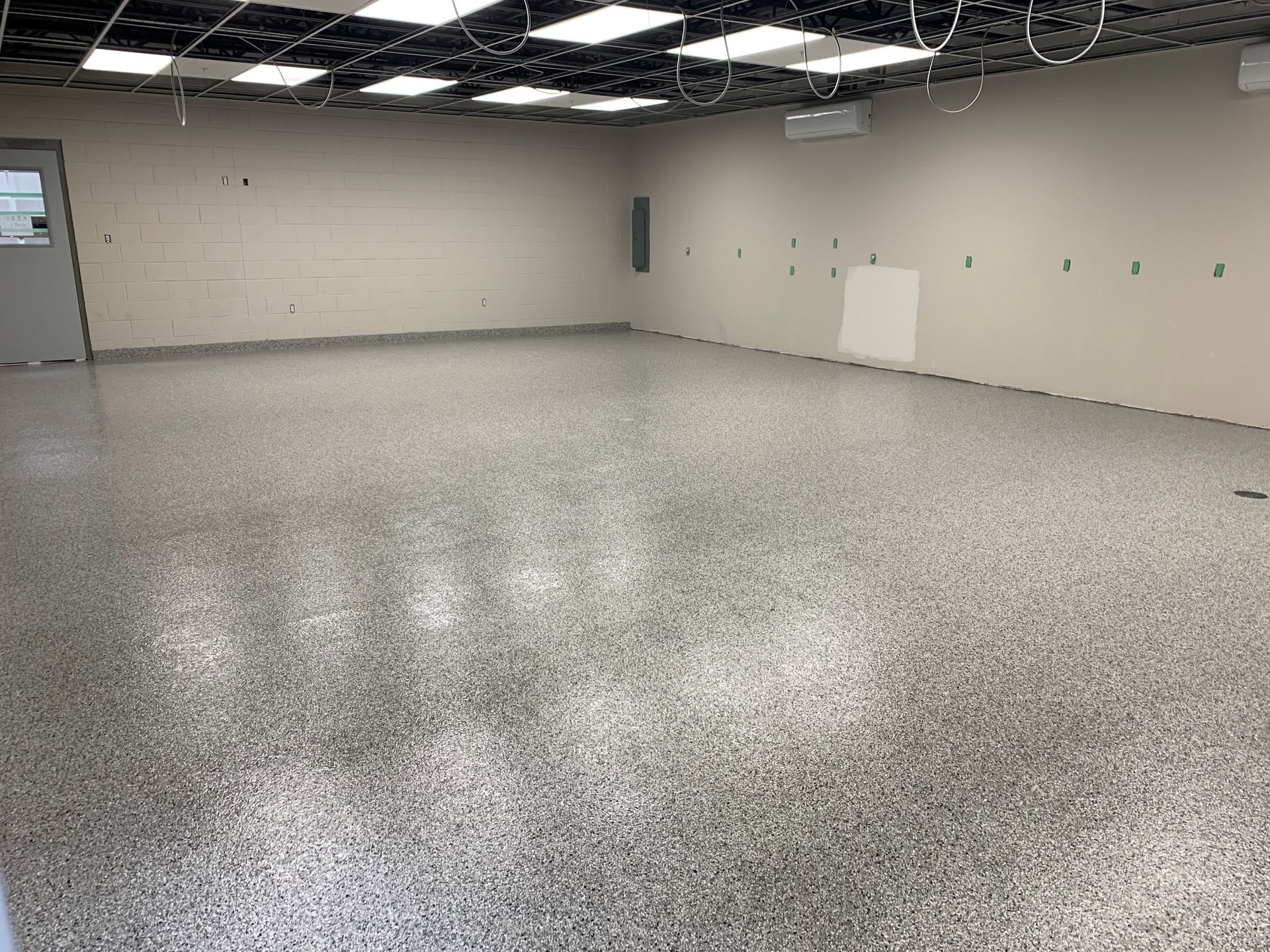 Empty indoor room with speckled floor, white walls, and exposed ceiling lights