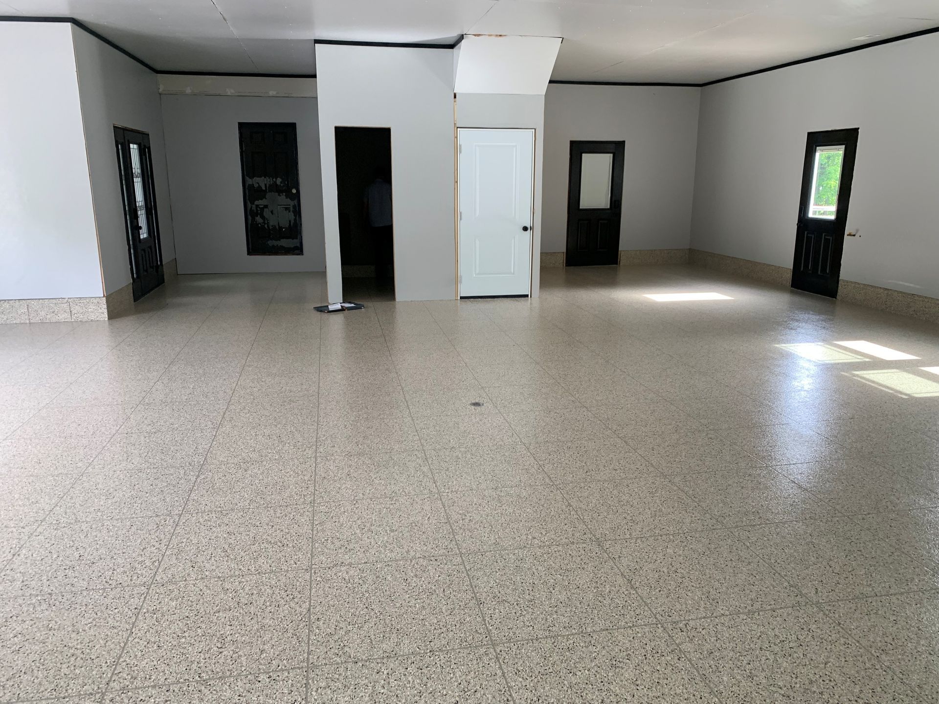 Empty room with speckled floor, white walls, black-framed windows, and a white door.