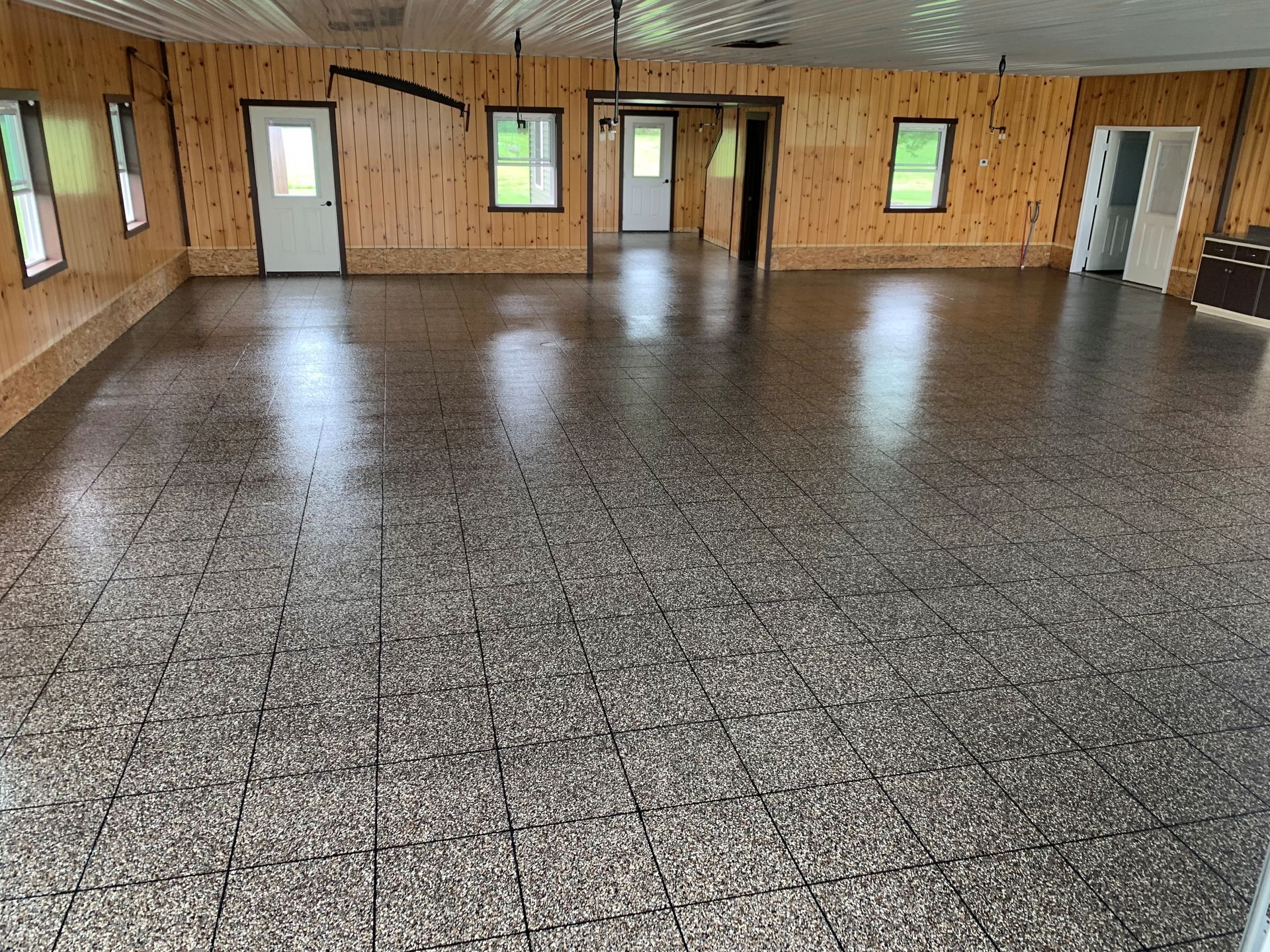 Empty hall with speckled tile floor, wood-paneled walls, windows, and several doors.