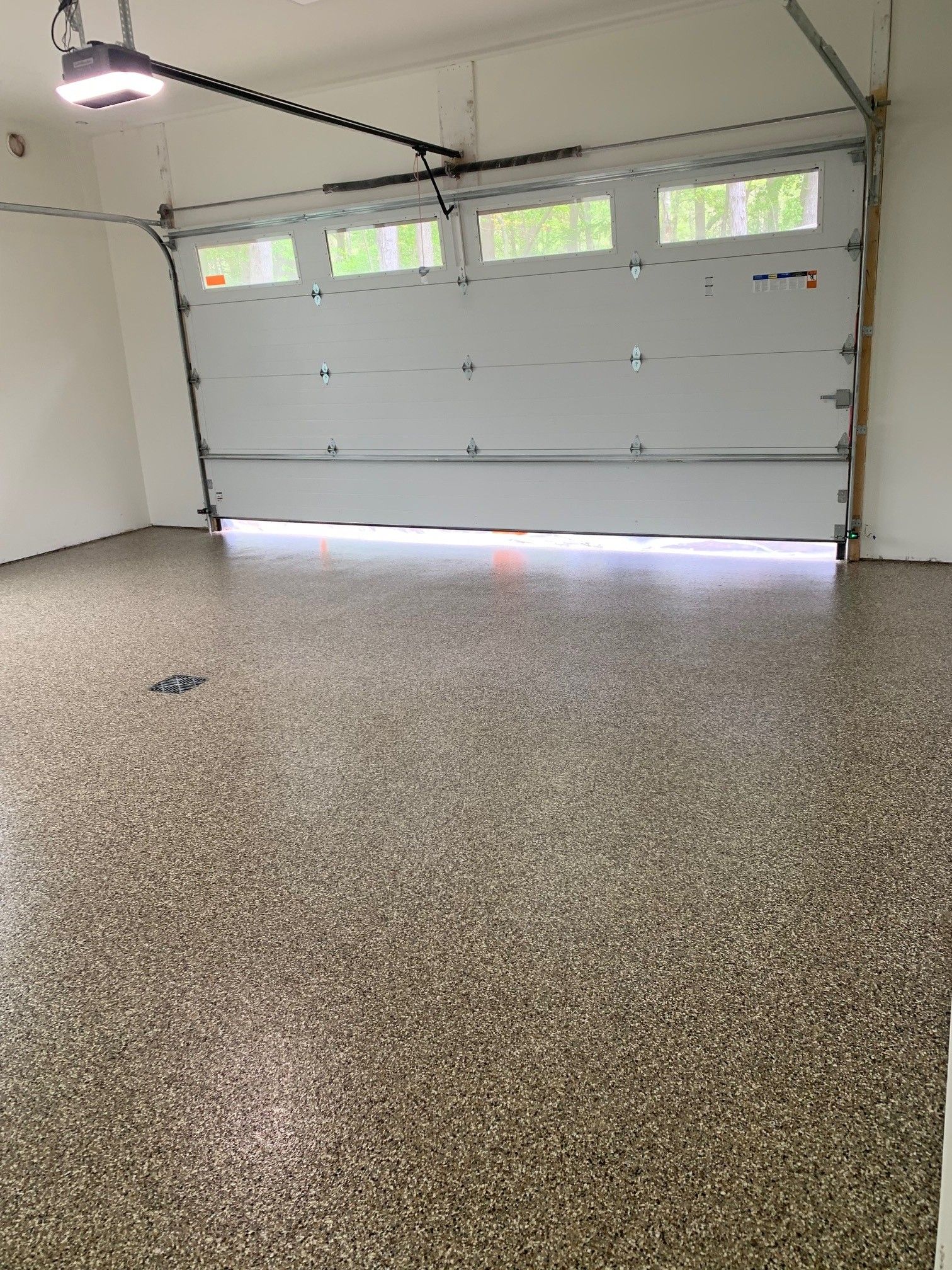 Empty garage with a closed gray sectional door and speckled epoxy floor.