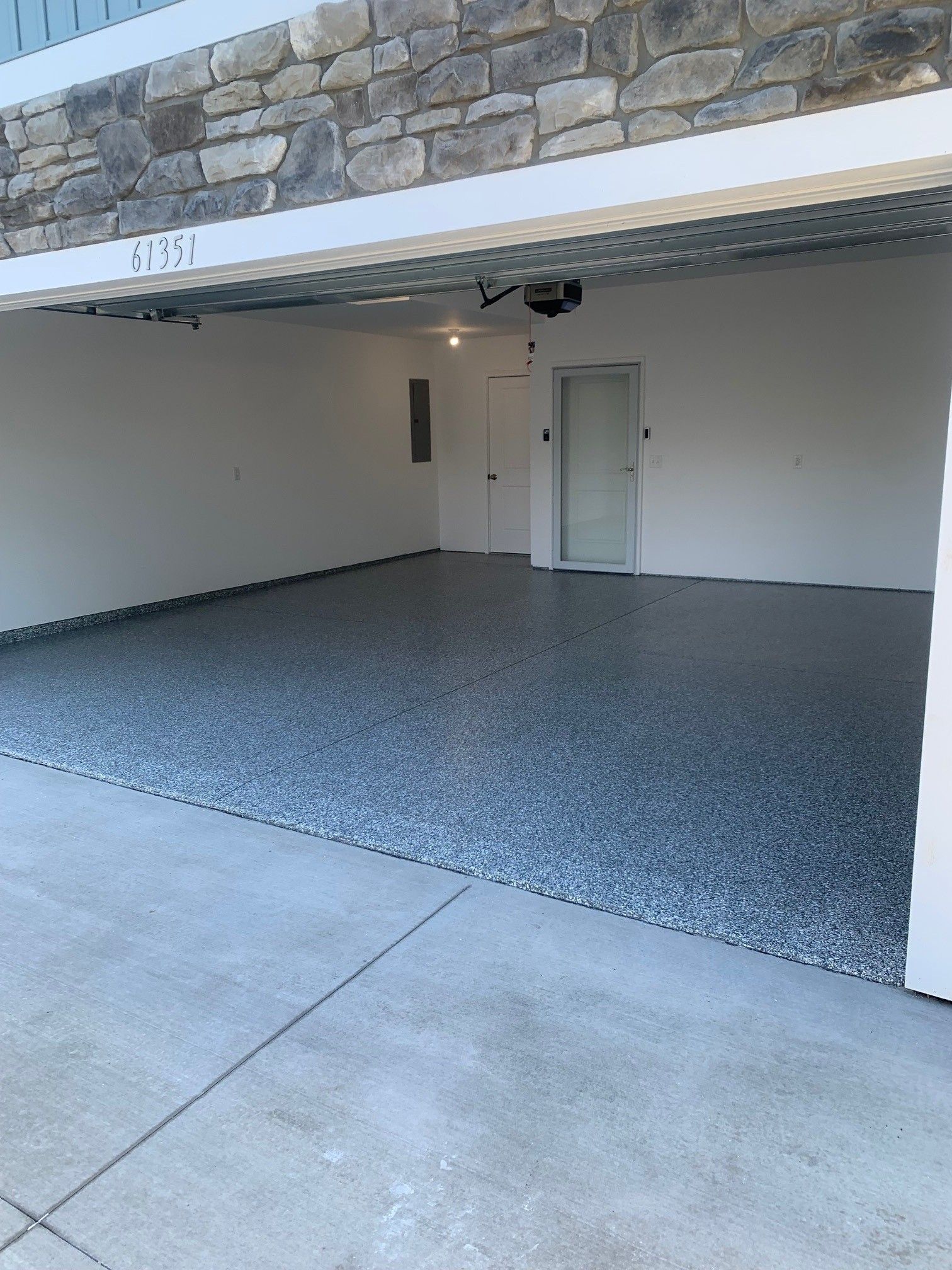 Empty residential garage with epoxy floor, white walls, and a closed side door.