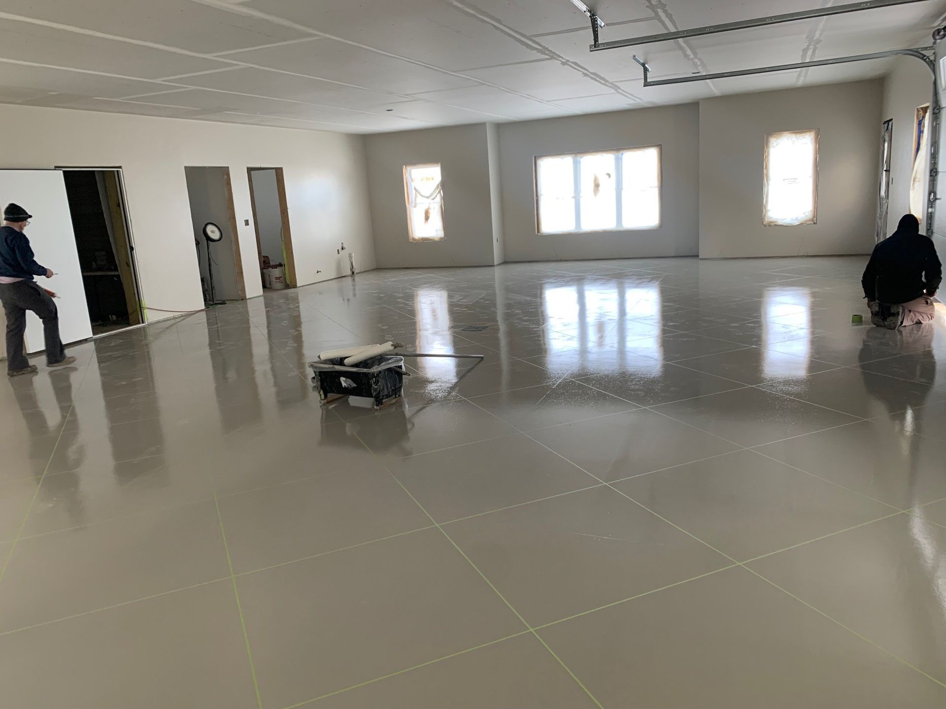 Empty tiled room with bright windows and a small cart in the center, two people near the walls