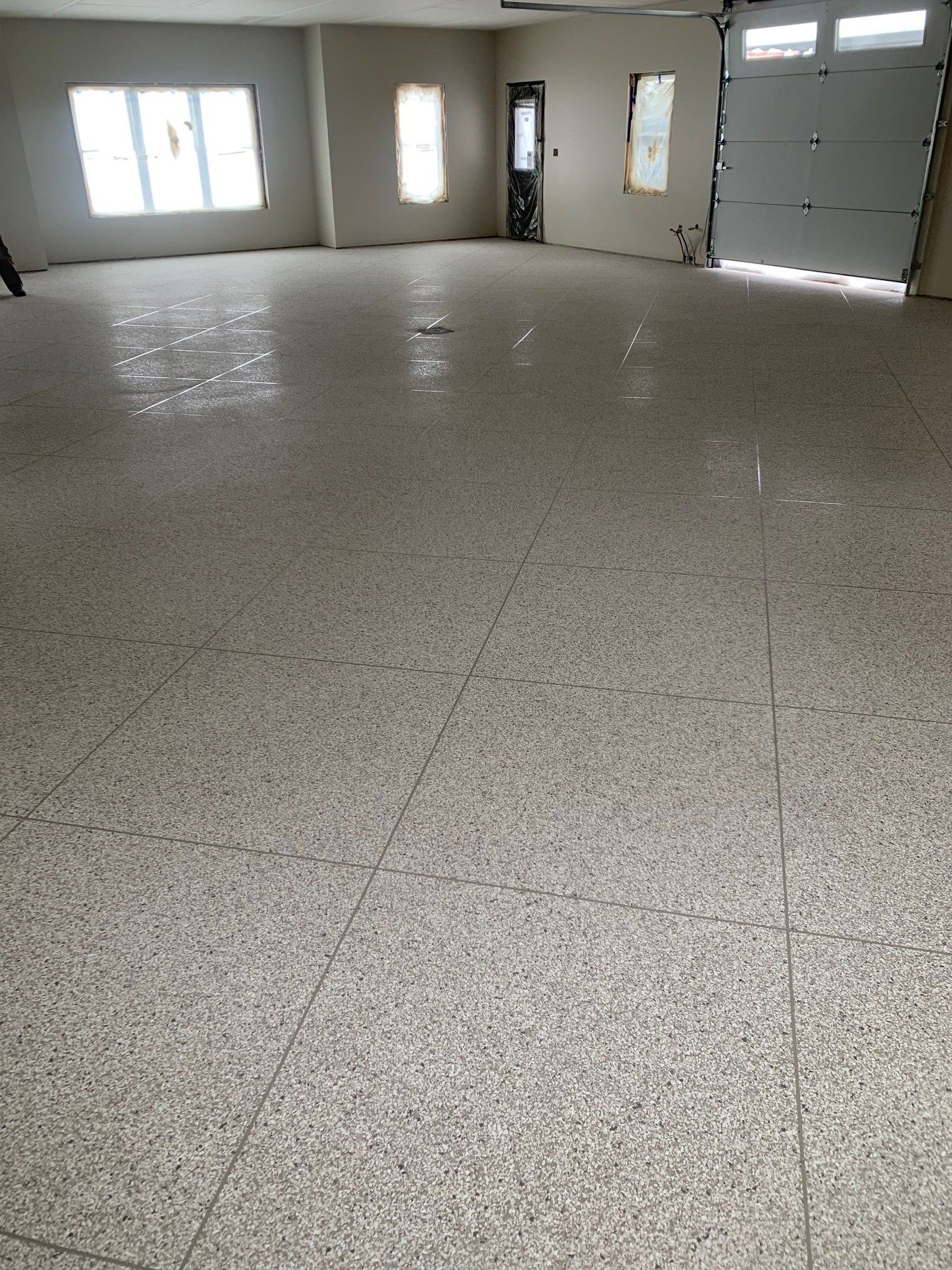 Empty garage interior with speckled floor, windows, and large garage door