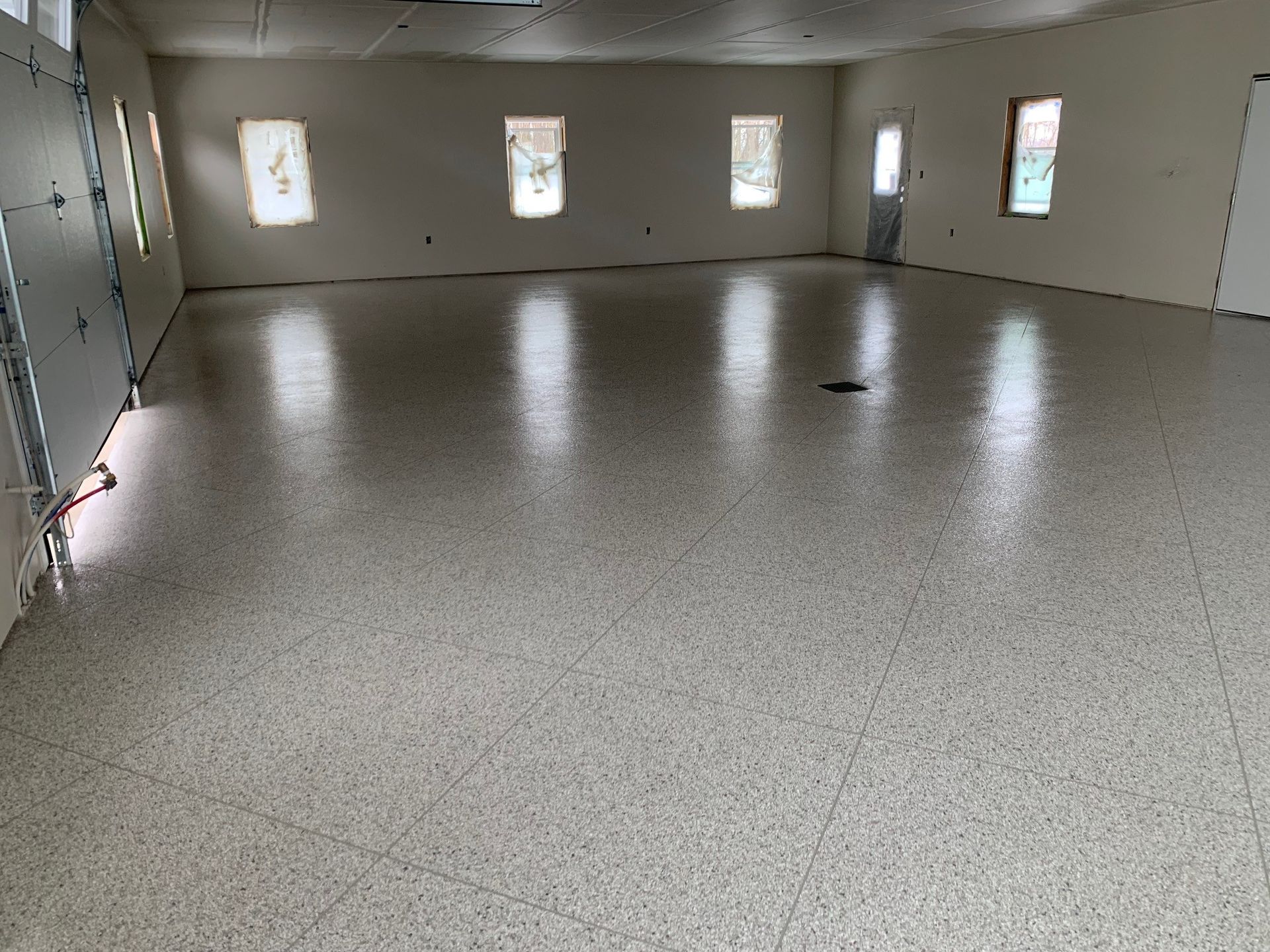 Empty garage with beige walls, small windows, and a speckled concrete floor