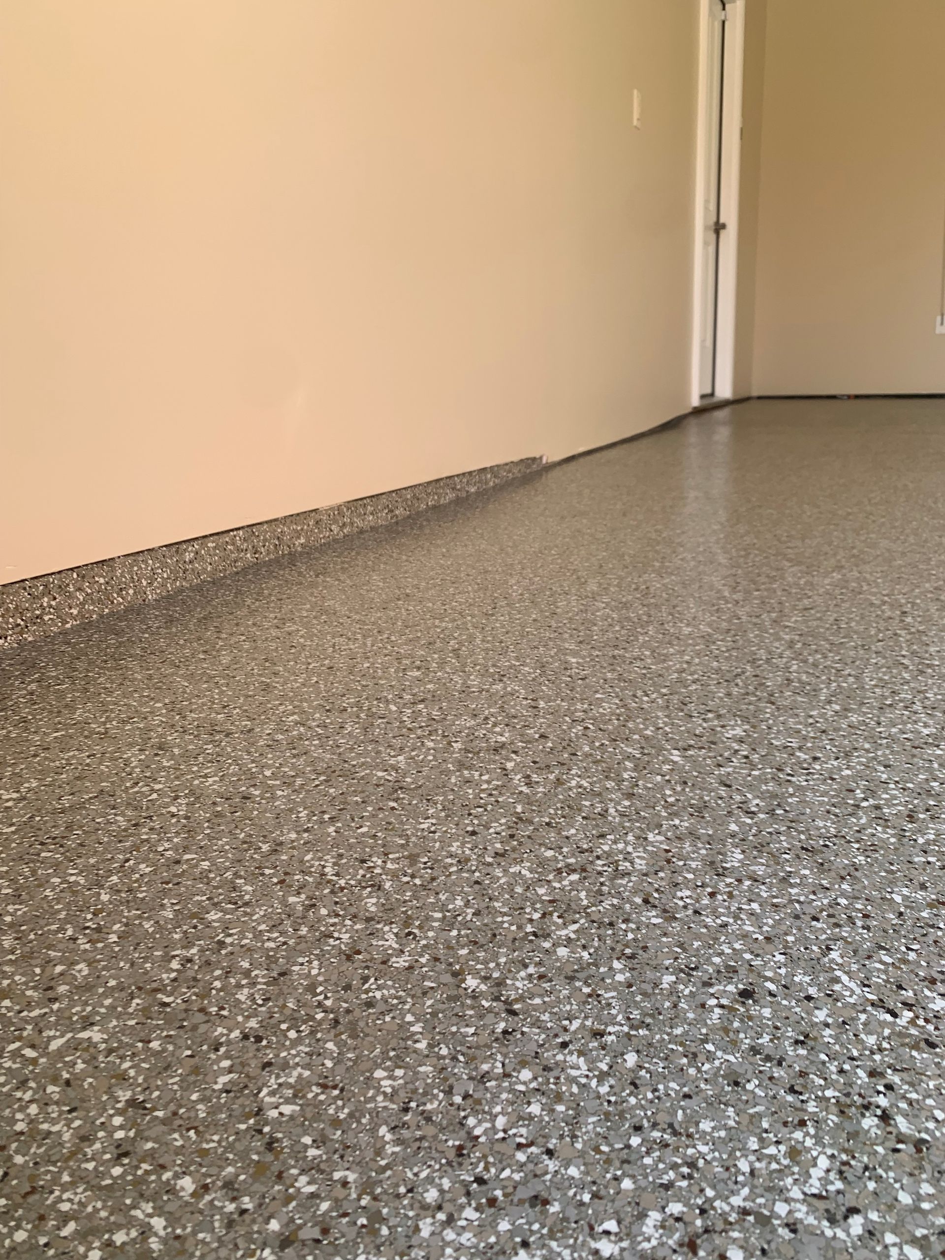 Speckled gray floor beside a beige wall and closed door in a hallway
