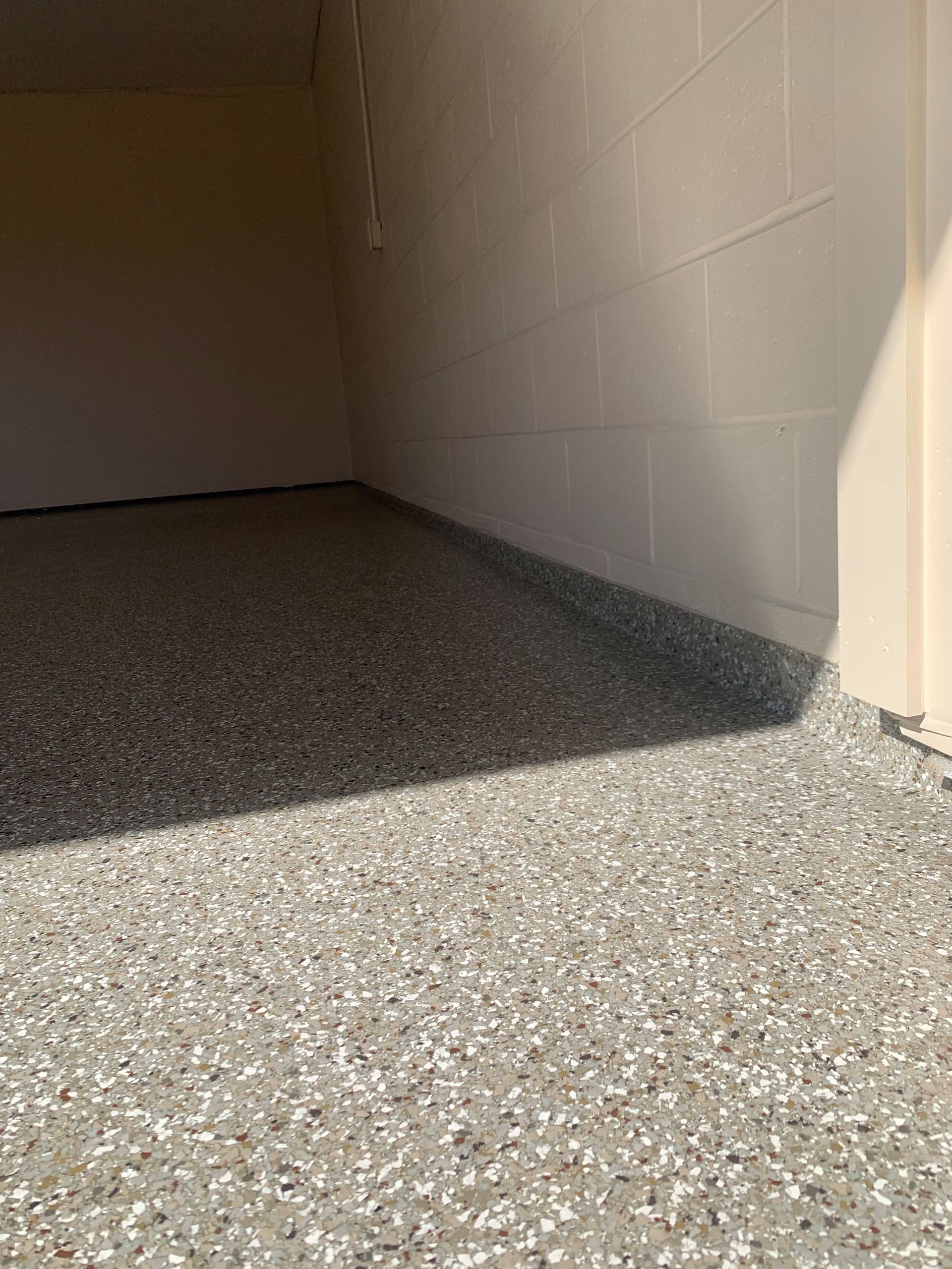 Empty concrete garage with speckled floor and white block walls, lit by sunlight from the right.