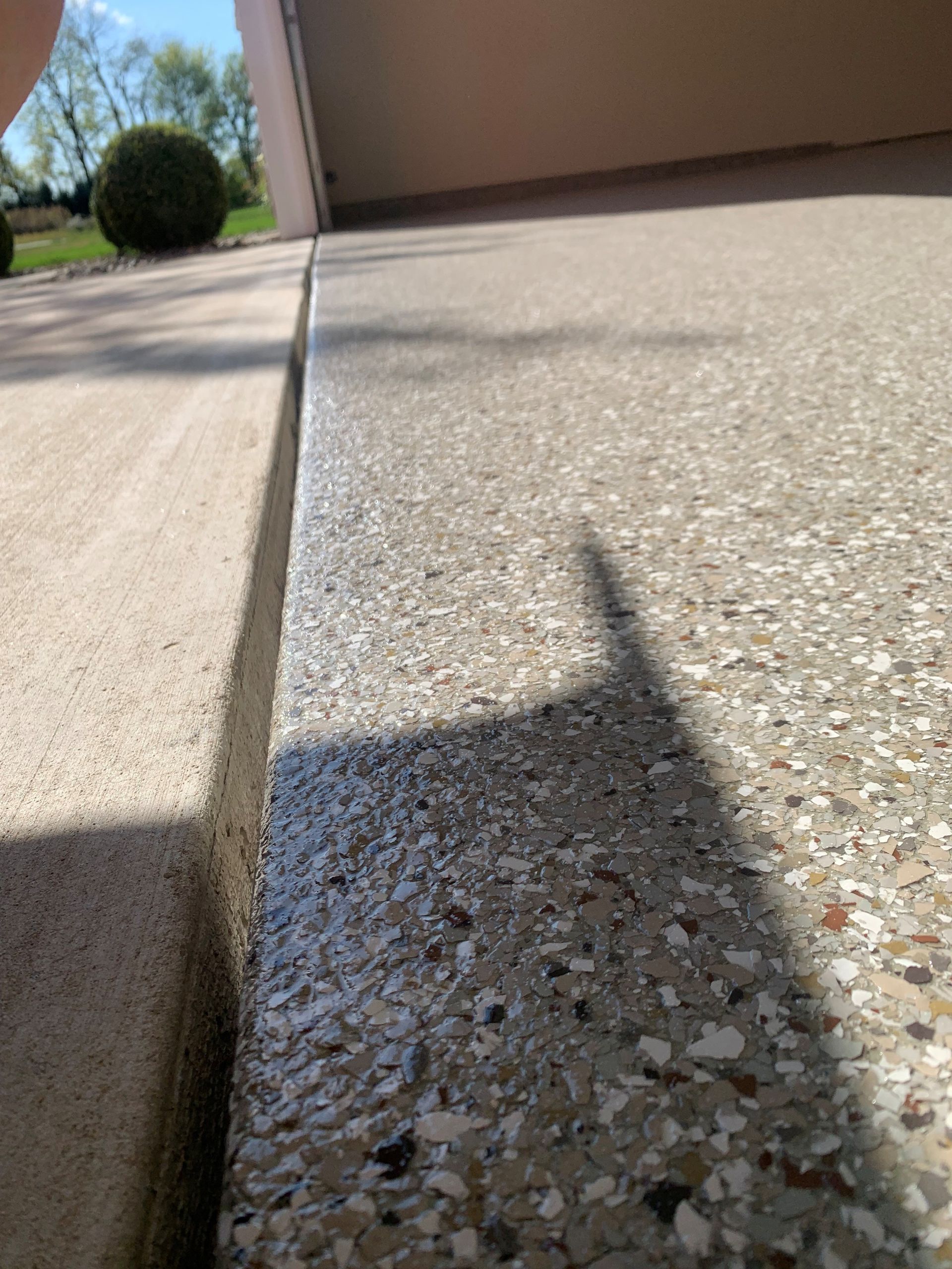 Low-angle view of a concrete sidewalk and curb beside a tan wall, with a plant and shadow in bright sun