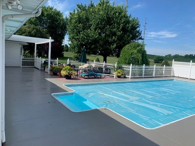 Backyard pool with blue cover, patio, lounge chairs, and white fence under a clear sky