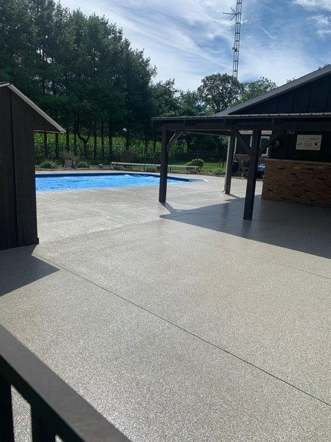 Empty pool deck with a blue swimming pool, covered pavilion, and trees in the background