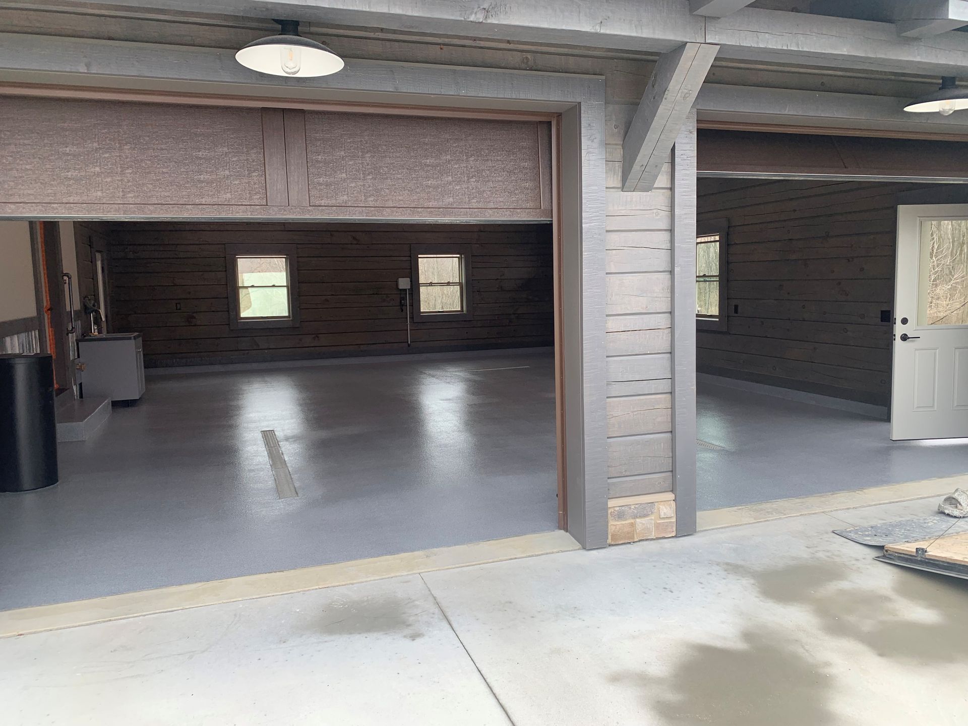 Open garage with gray concrete floor, wood-paneled walls, and overhead lights.
