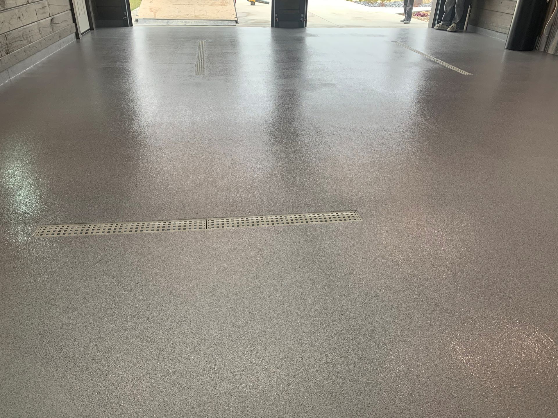 Textured gray concrete floor in an indoor hallway, with a narrow drainage grate running across it.