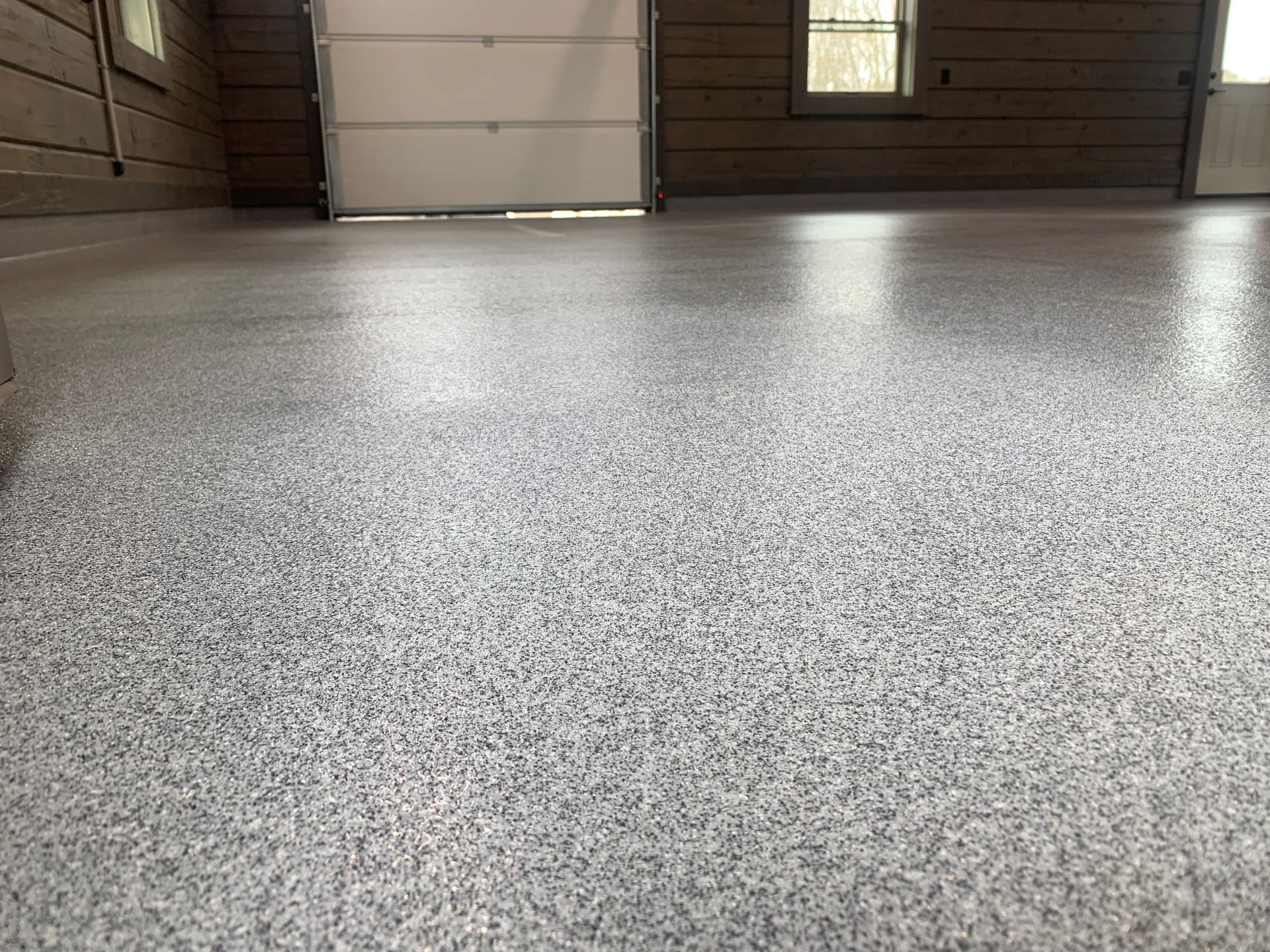 Empty garage floor with gray speckled epoxy coating and closed door in the background