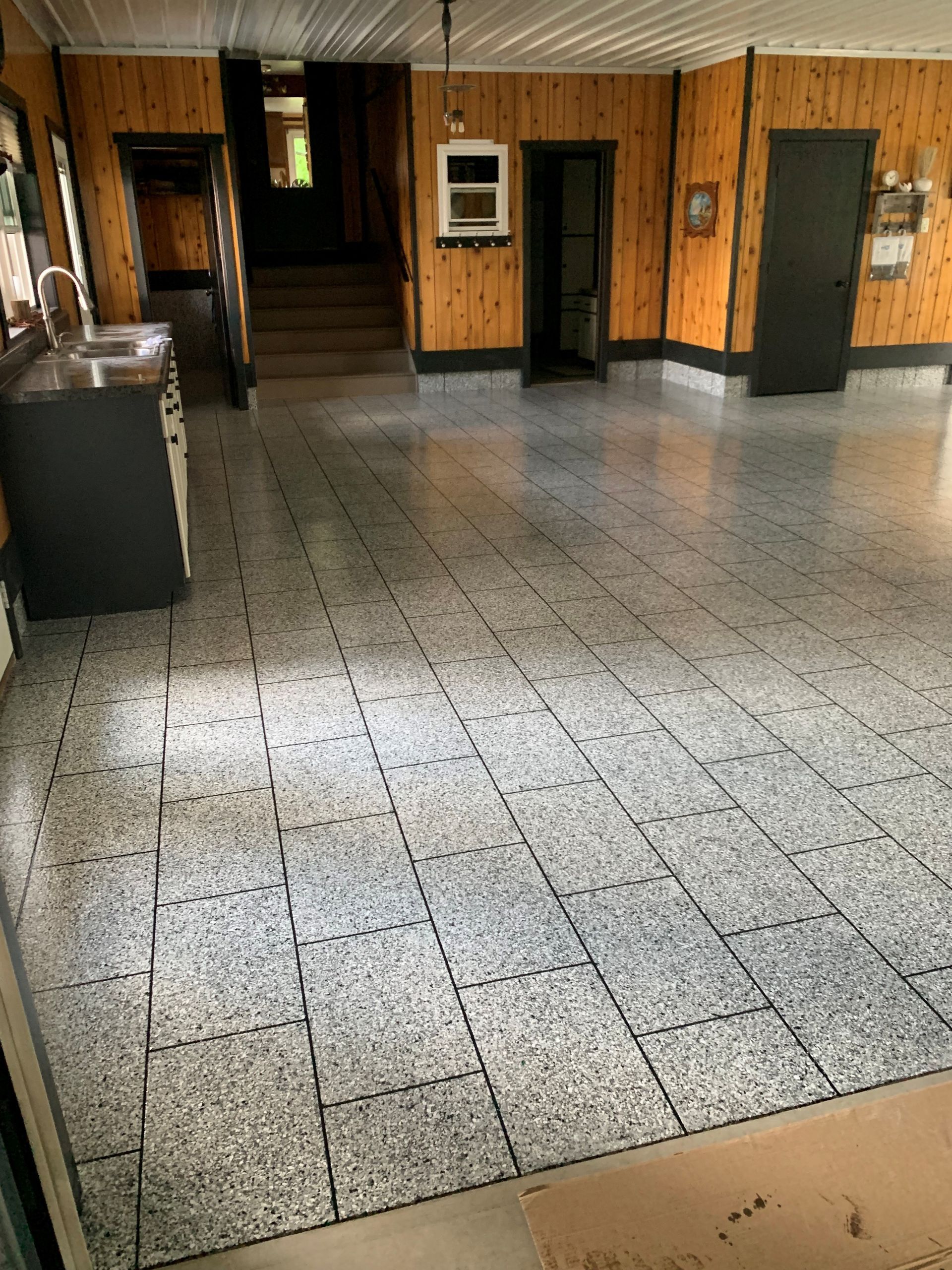 Empty room with speckled tile floor, wood-paneled walls, and a sink area on the left.