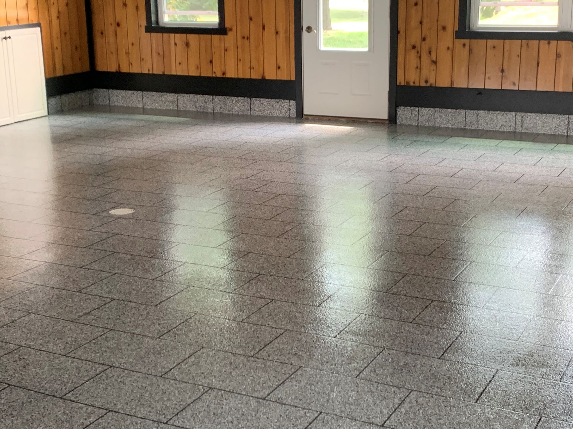Empty tiled room with wood-paneled walls and a doorway, reflecting light on the floor.