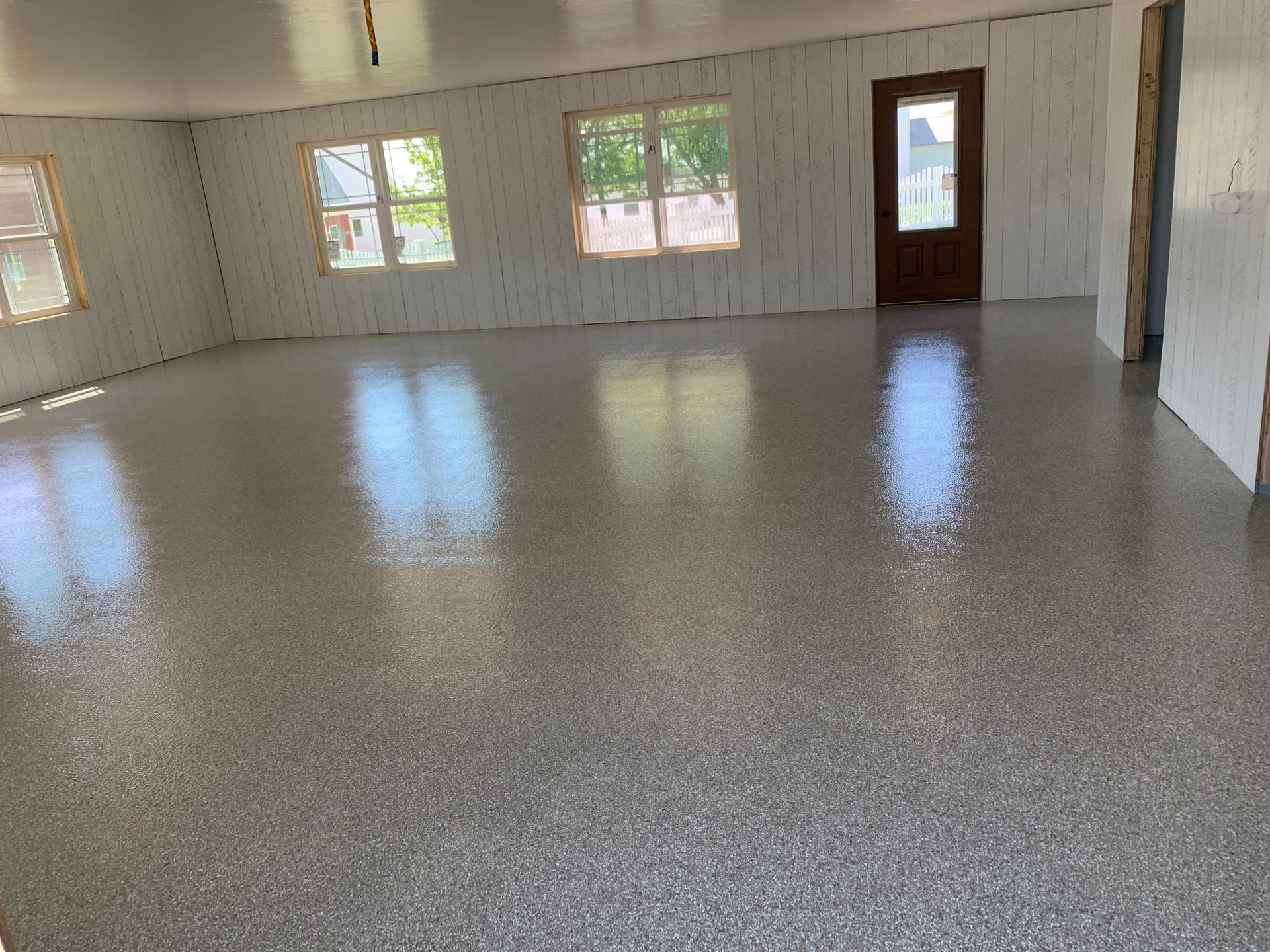 Empty room with white walls, speckled floor, windows, and a wooden door.