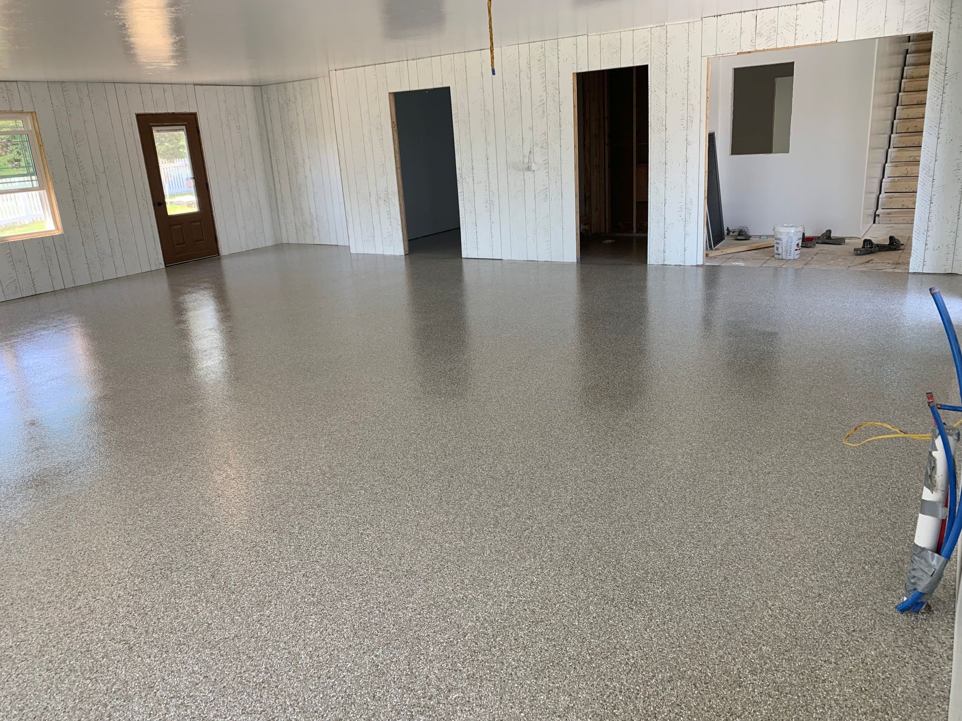 Empty unfinished room with white walls, multiple doorways, and a gray speckled floor