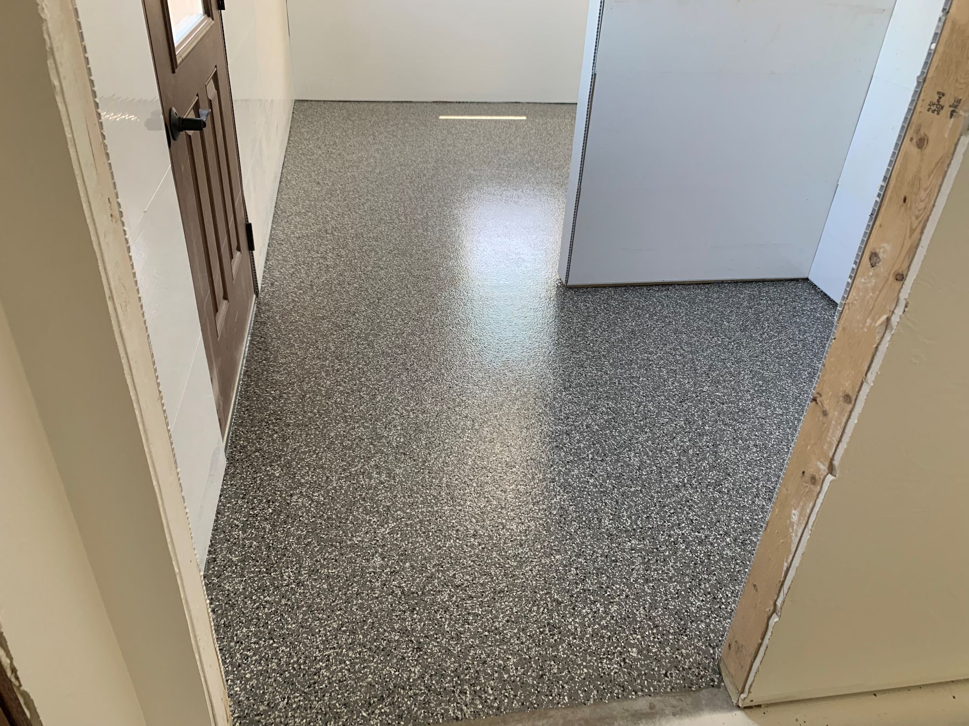 Small hallway with speckled gray flooring, white walls, and open doorways.