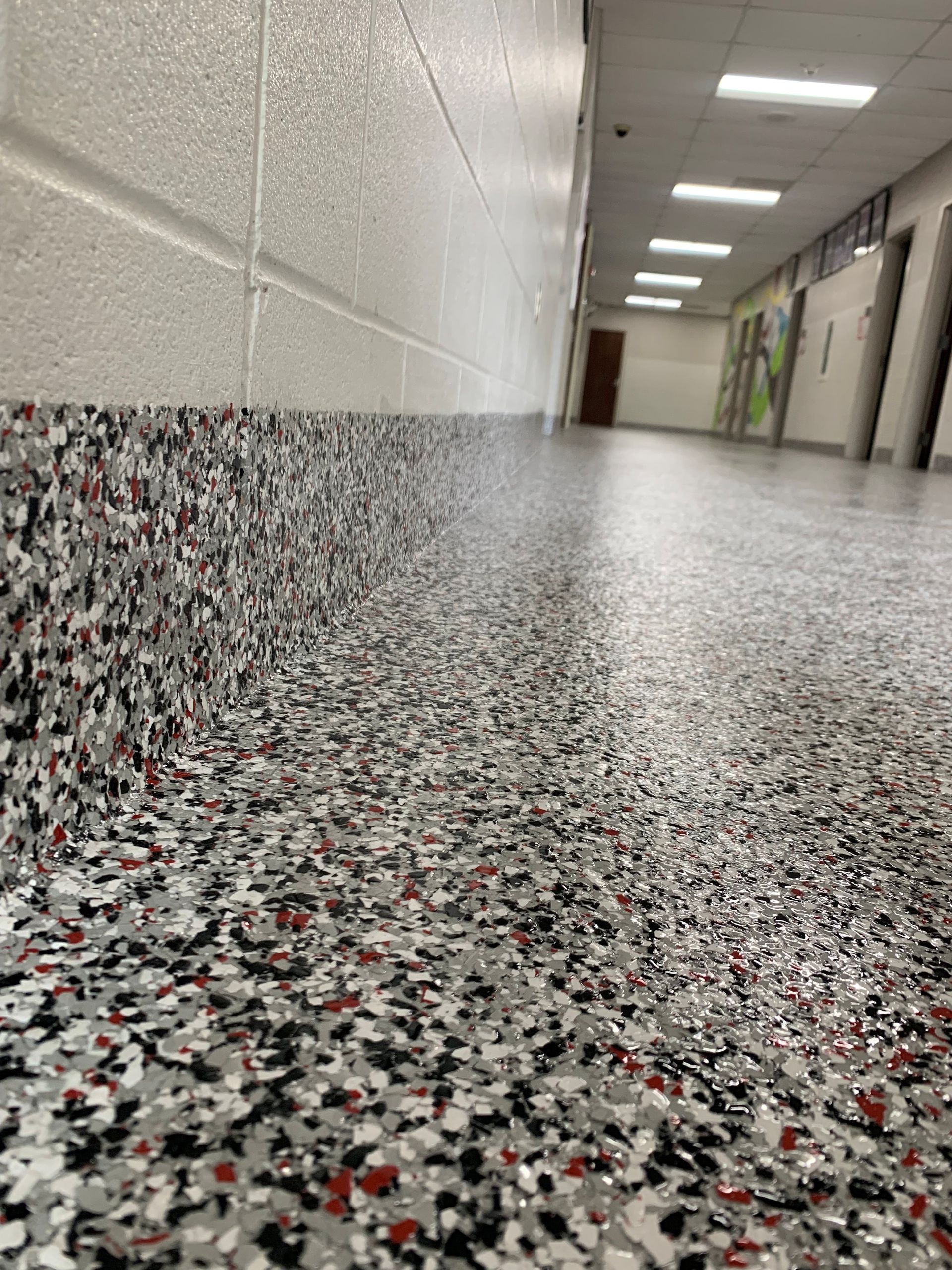 Low-angle view of a hallway with terrazzo floor, white walls, and ceiling lights leading to doors in the distance