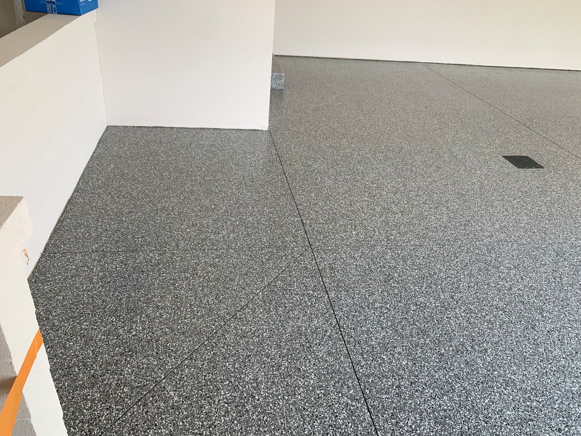 Empty speckled gray carpeted floor beside white walls and a small black floor mark