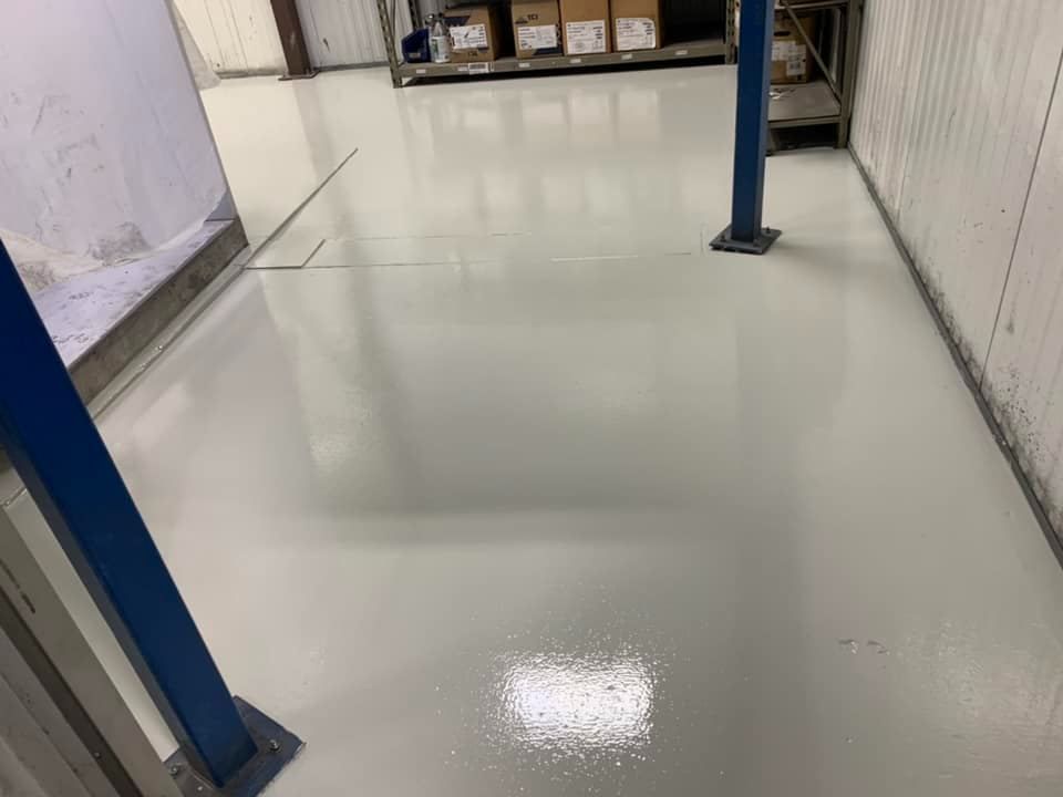 White epoxy floor in an industrial room with blue support columns and shelves in the background