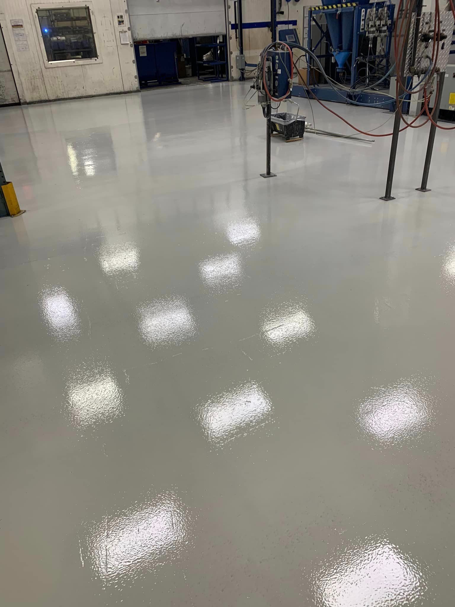 Shiny white factory floor with reflections, blue machinery, and equipment in the background.