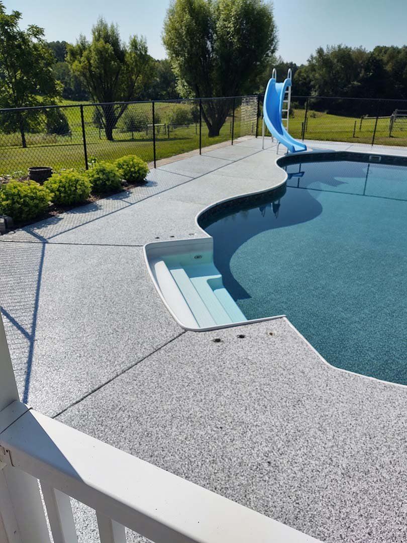 Backyard pool with built-in steps and a blue slide, bordered by a white concrete deck and green lawn