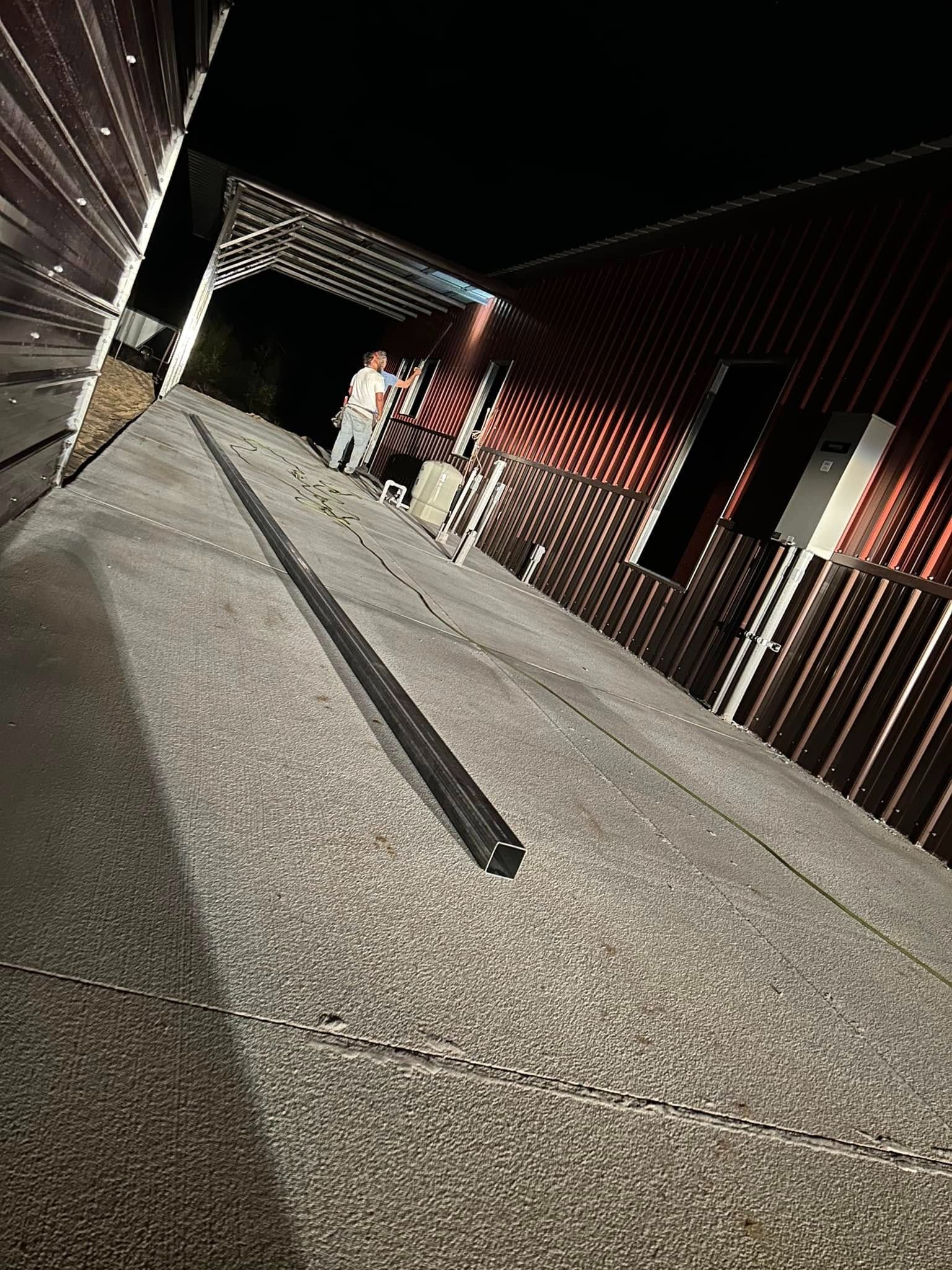 A low-angle night view shows a person walking toward a modern industrial building with dark corrugated metal walls.