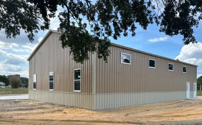A tan metal building with light-colored wainscoting and several windows, set against a blue sky with scattered clouds.