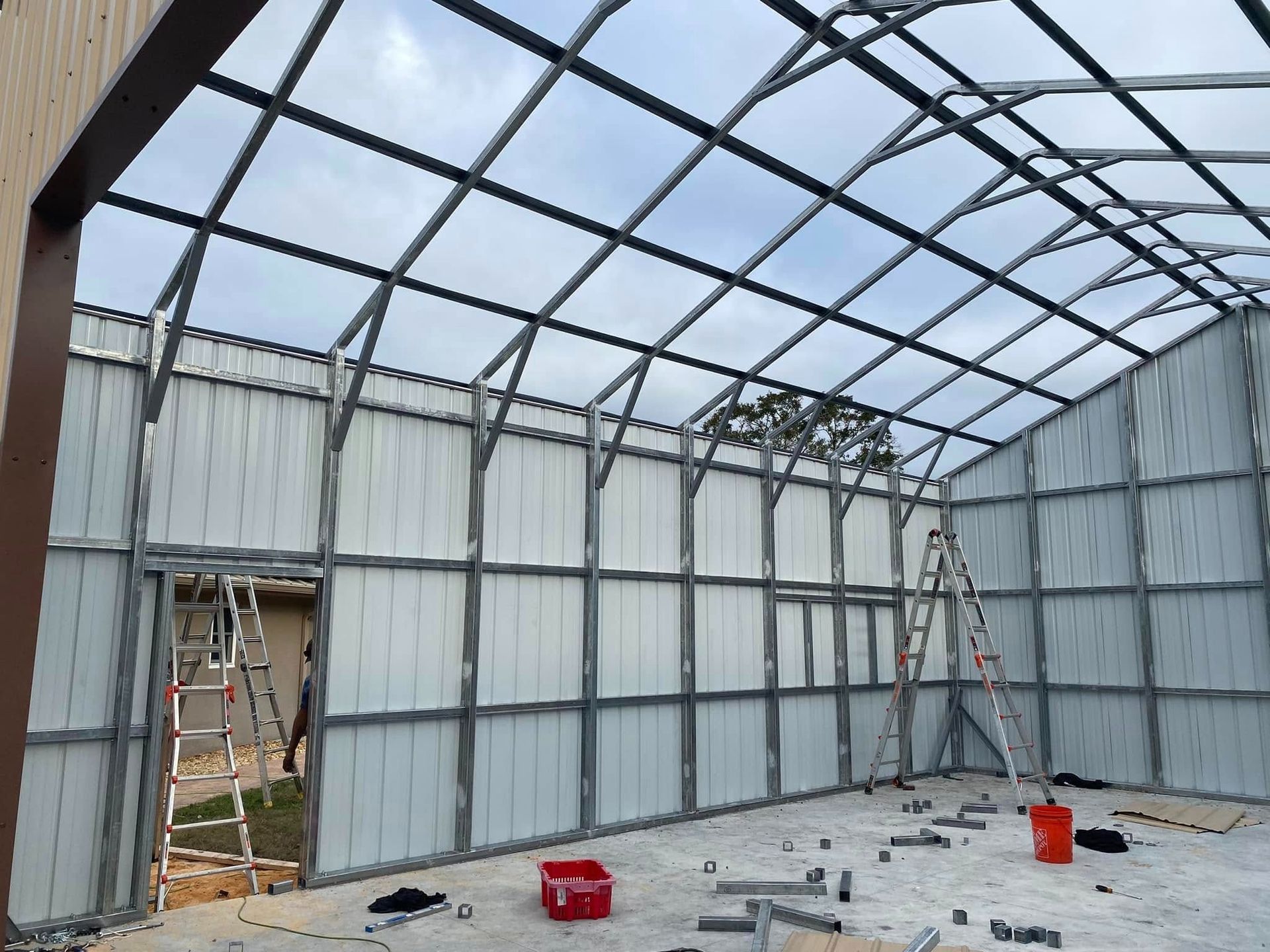 Interior view of a partially constructed metal building with steel framework and wall panels, featuring ladders on site.