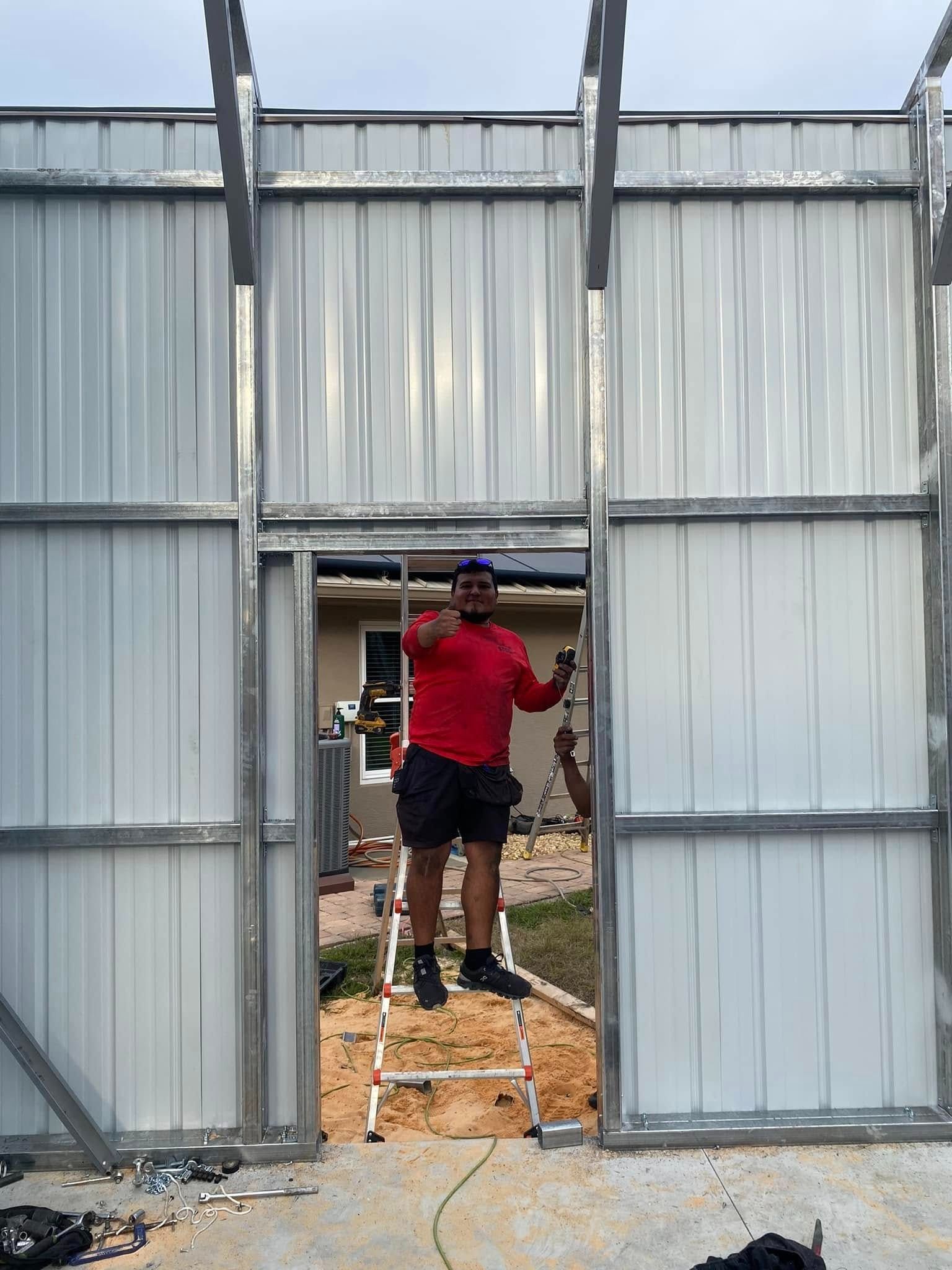 A person in a red shirt stands on a stepladder in the doorway of a metal frame wall under construction.