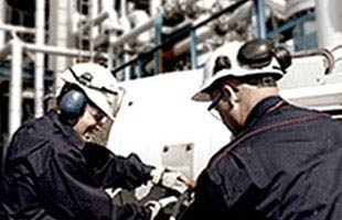 Two workers in safety gear inspect machinery in an industrial setting