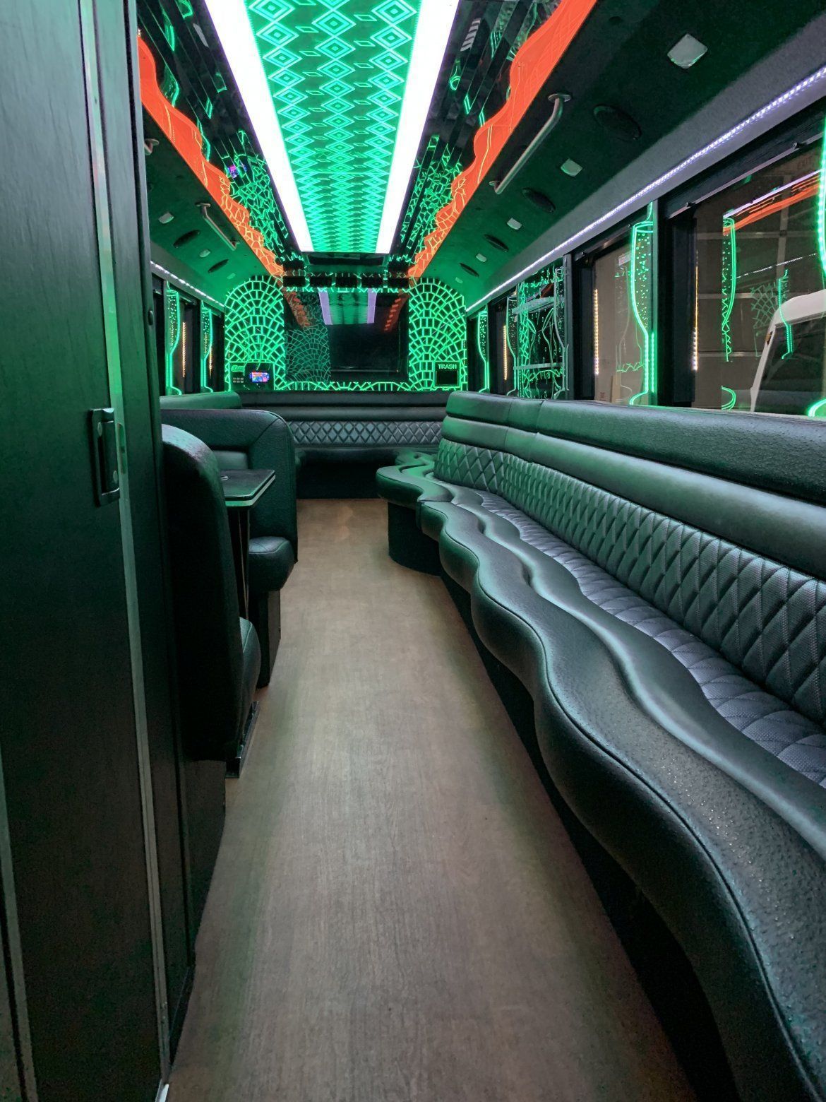 Interior of a party bus with green and black leather seating, a mirrored ceiling, and wood-look flooring.