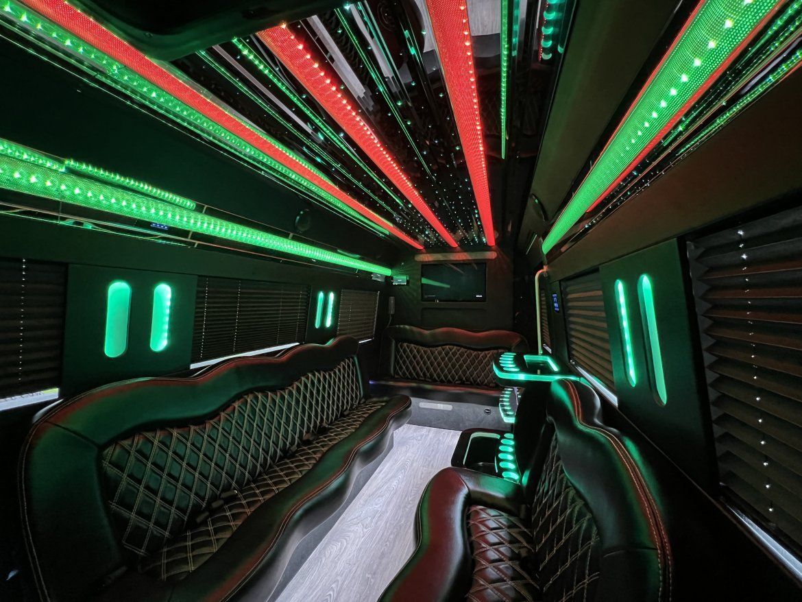 Interior of a luxury black limousine with green and red LED lights and black diamond-stitched leather seating.