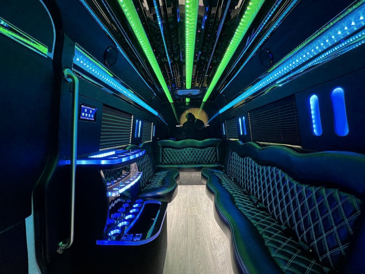 Interior of a luxury limousine, dark with neon blue and green lights illuminating seating and ceiling.