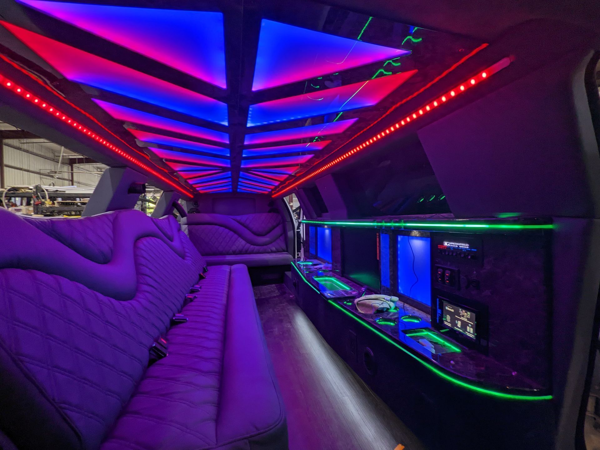 Interior of a limousine with purple, blue, and red LED lighting. Black countertops and seating.