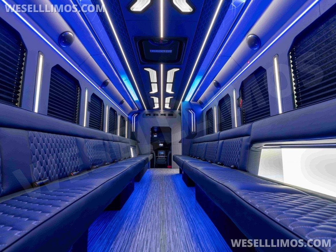 Interior of a blue lit party bus with leather seating, windows, and overhead lighting.