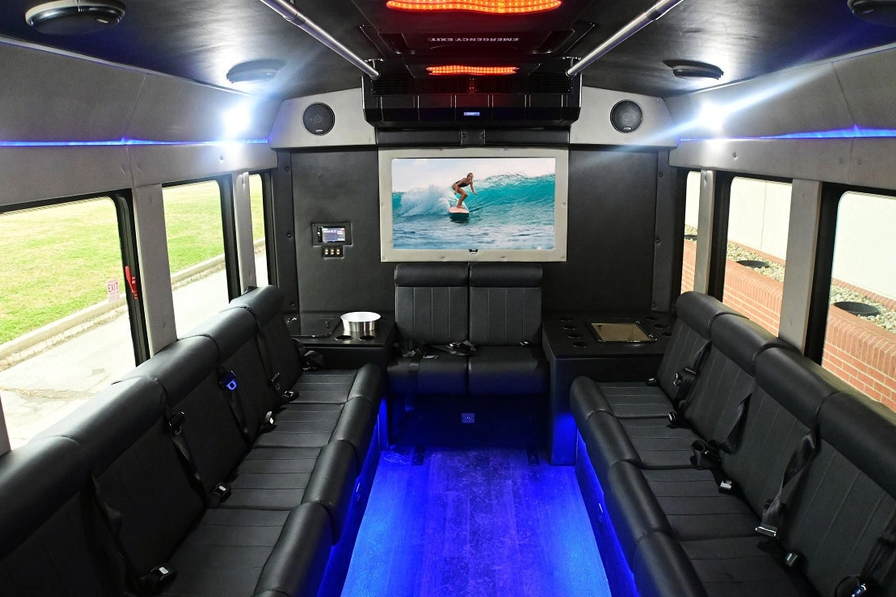 Interior of a party bus with black leather seating, TV, and blue LED lighting.