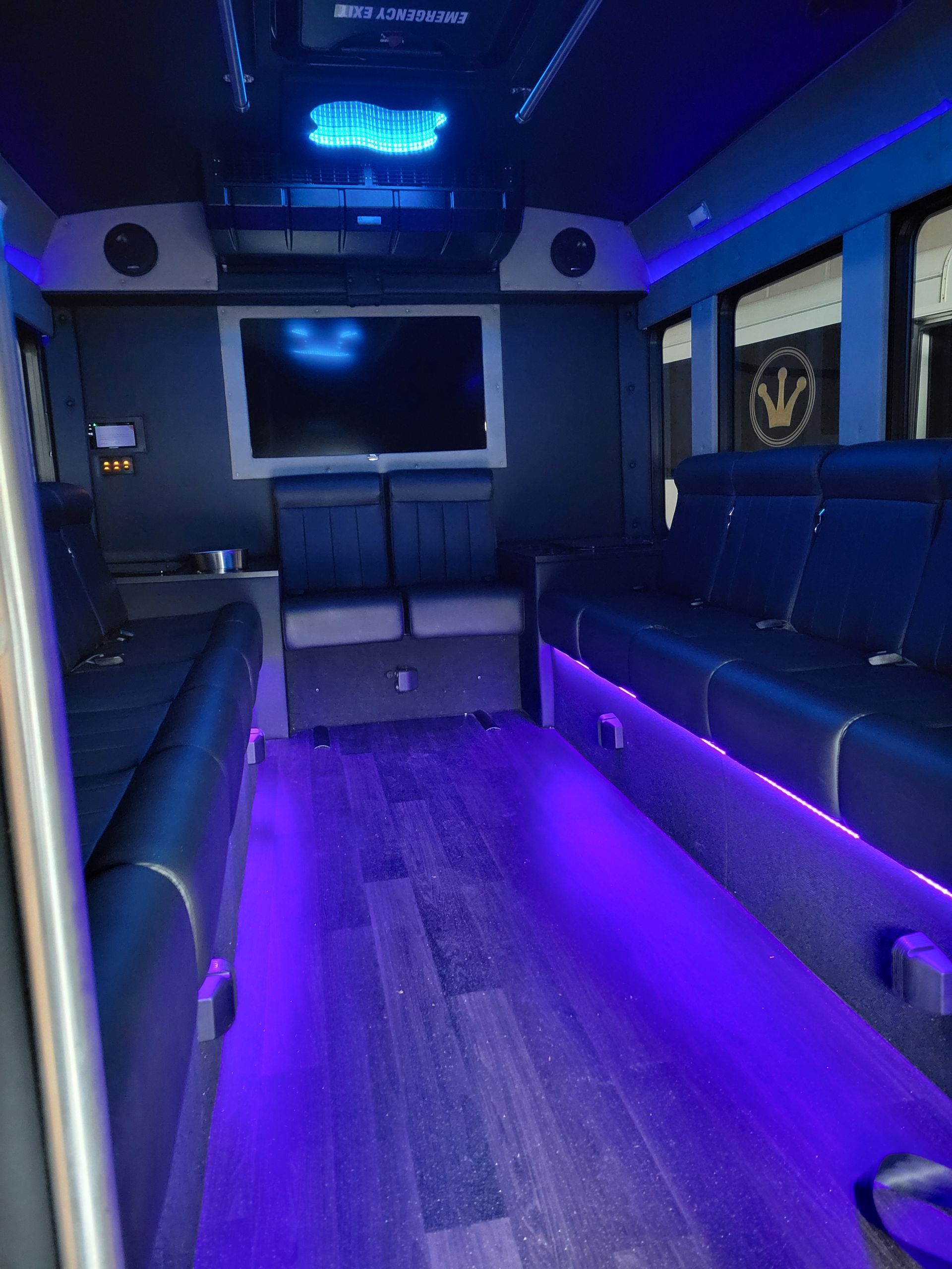 Interior of a party bus with black leather seating, a TV, and blue LED lighting.