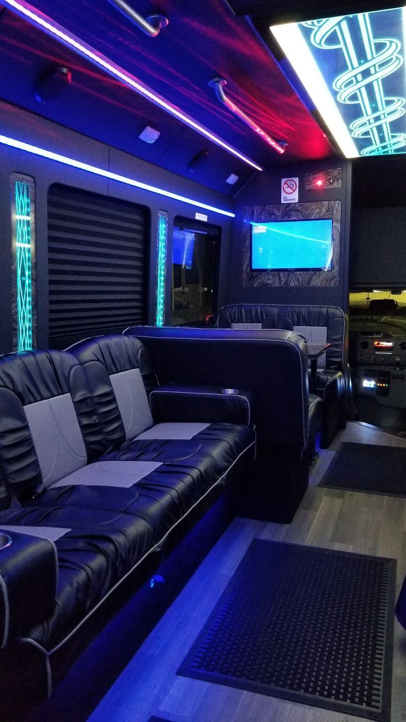 Inside a luxury party bus with black leather seating, neon lights, and a TV.