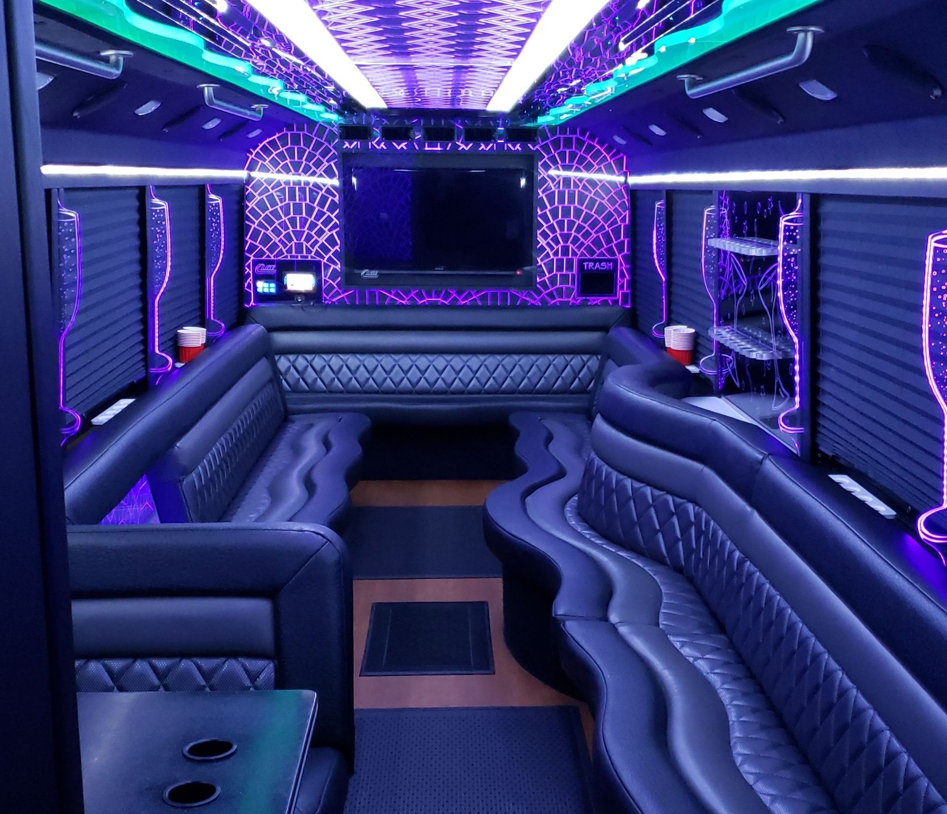 Inside of a luxury party bus; seating, bar, and TV illuminated in blue and purple.