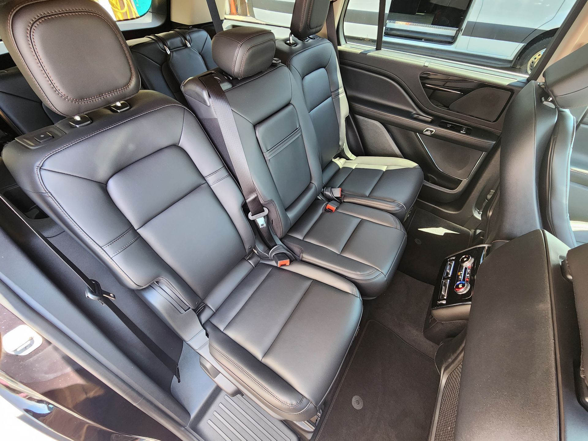 Black leather third-row seats inside a car with headrests and seatbelts, viewed from a slight angle.