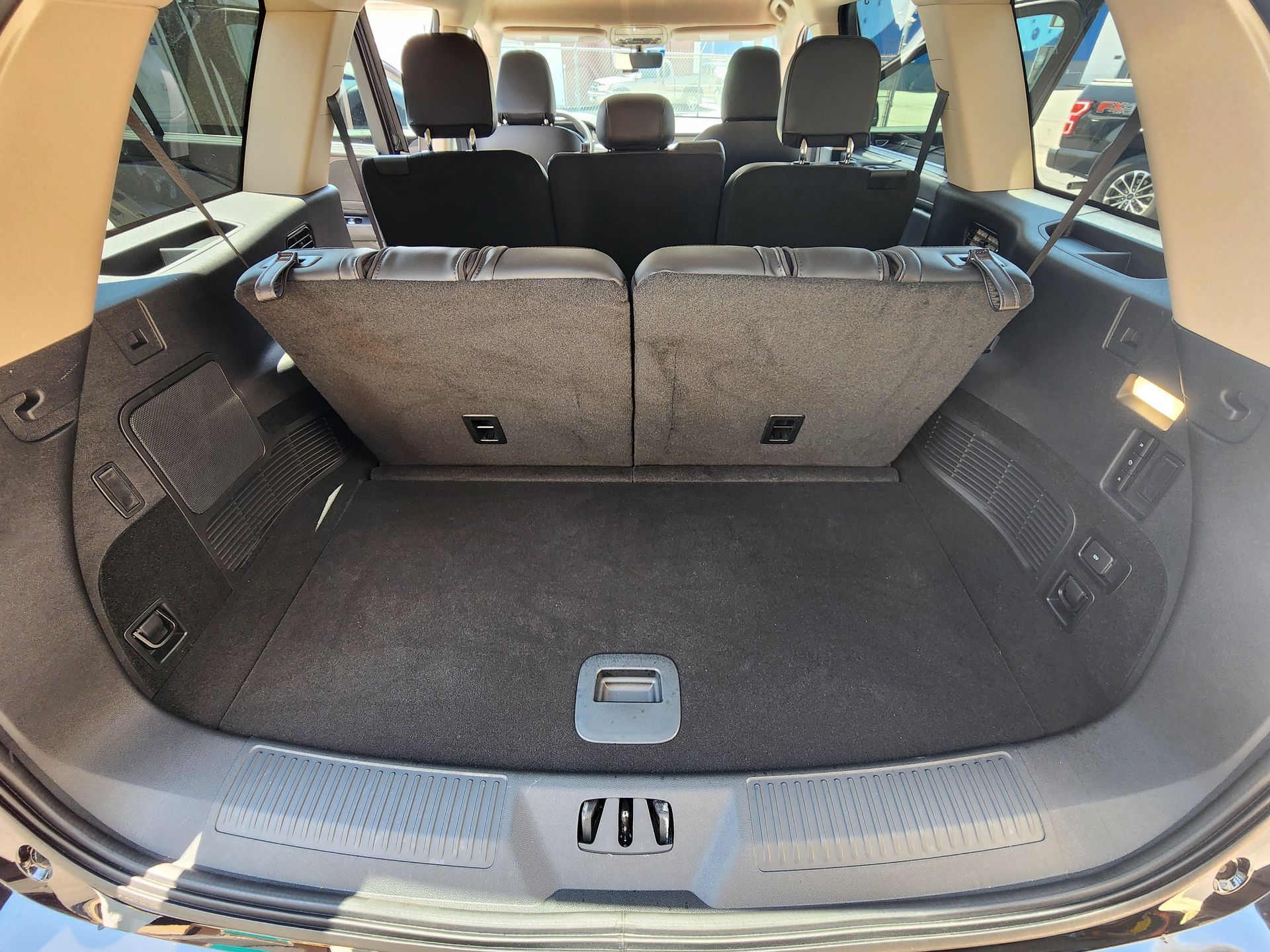 Empty cargo area of a car with folded rear seats, black carpet, and side storage compartments.