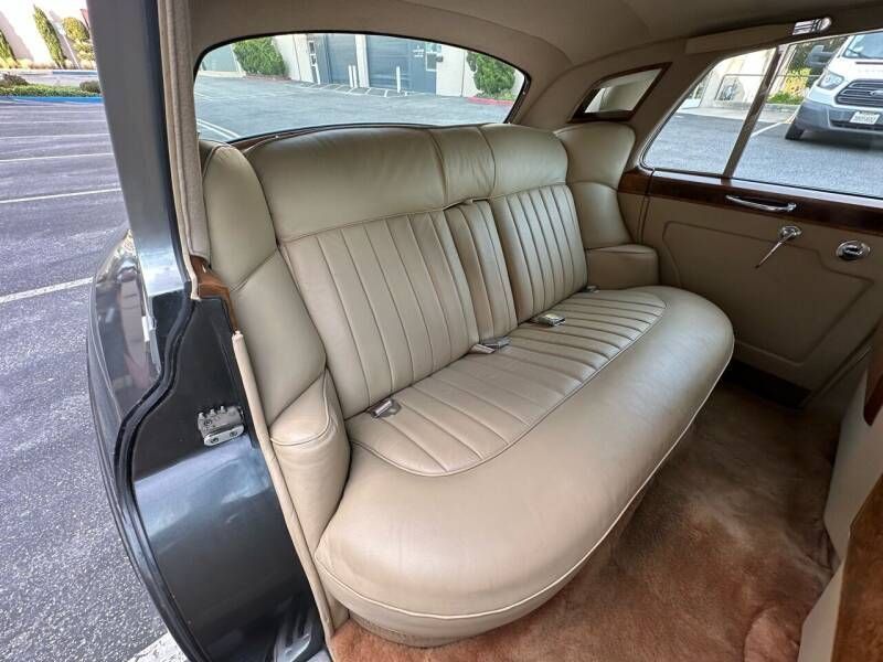 Beige leather interior of a classic car, showing a back seat with wood trim and a window.